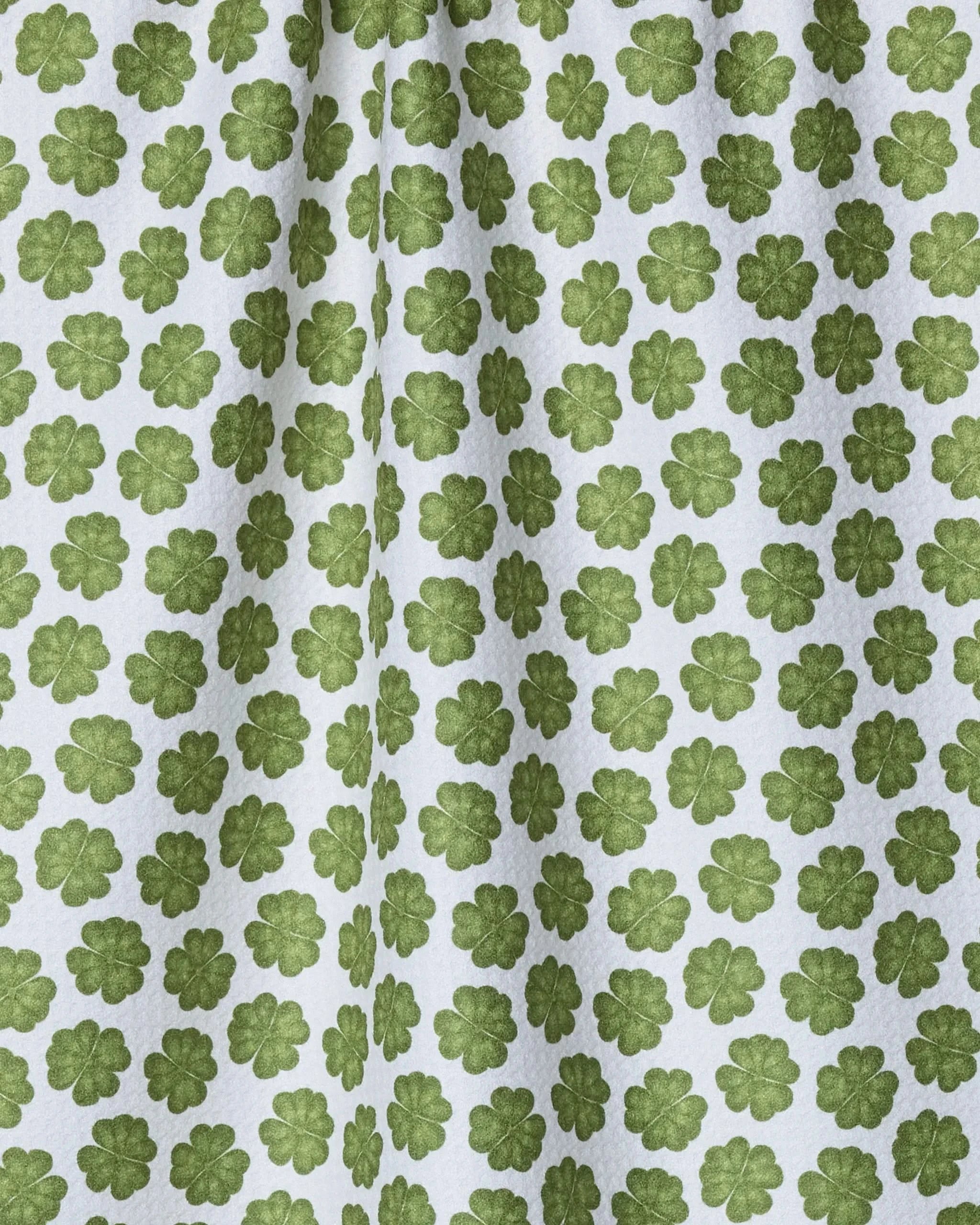 The Geometry Patty is a white recycled kitchen towel featuring a repeating green four-leaf clover pattern. Its fabric displays subtle folds and shadows for a textured look.