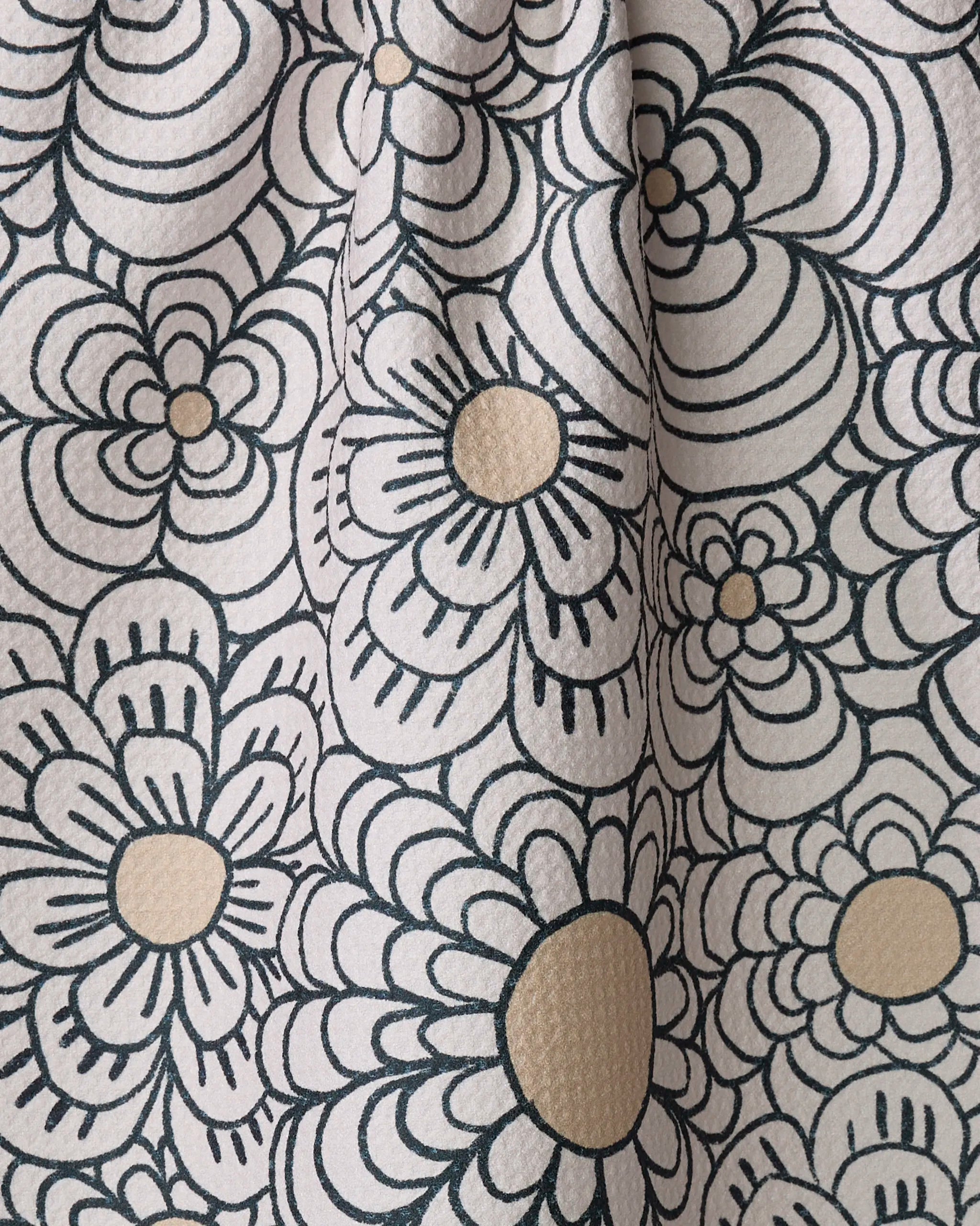 Close-up of Paulette, a recycled kitchen towel by Amy MacCready, showing a black and white floral pattern with large outlined flowers, tan centers, overlapping petals, and visible textured folds with shadow details.