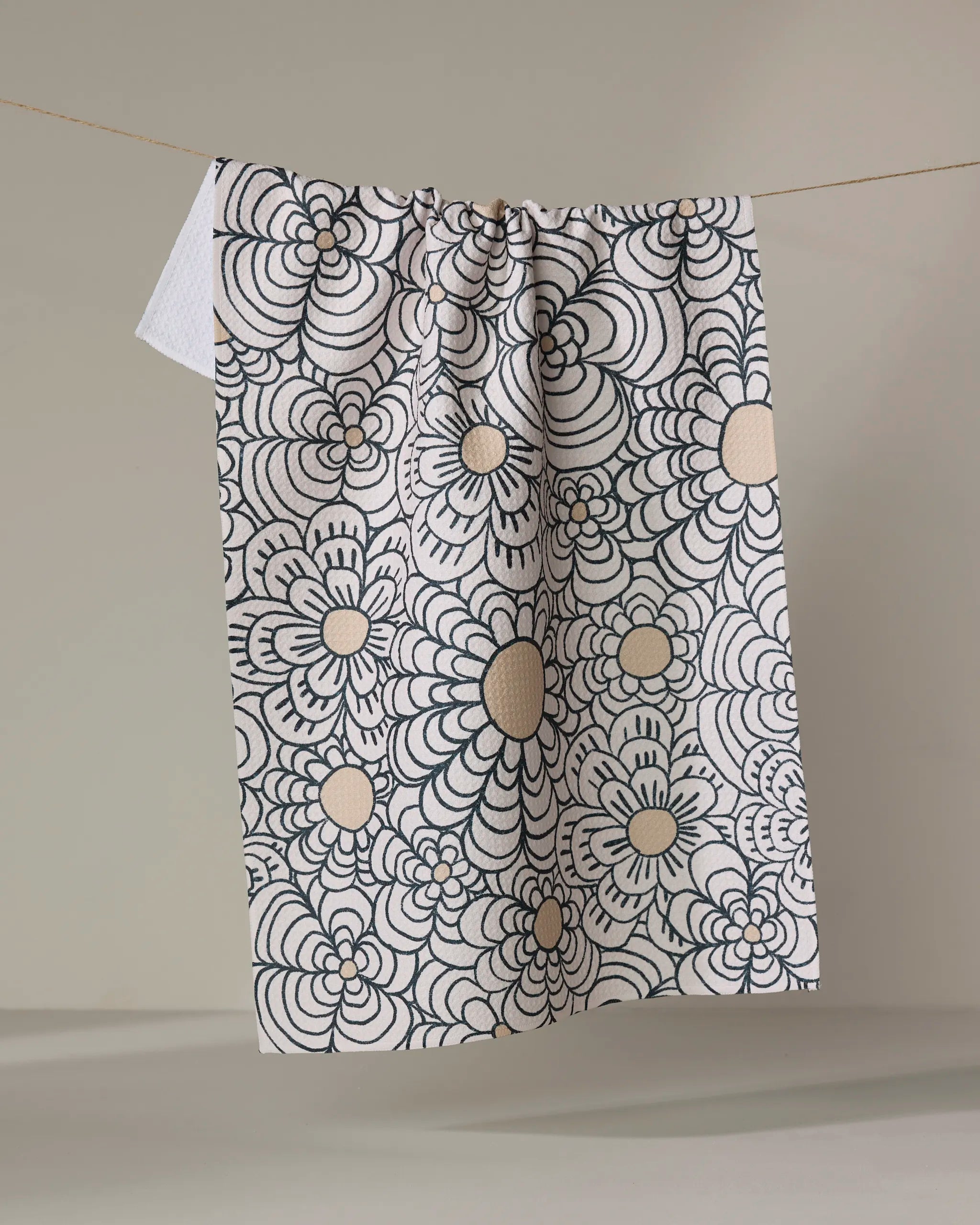 The Paulette towel by Amy MacCready showcases a bold black floral pattern with large, overlapping flowers and hangs from a clothesline against a plain, light background.
