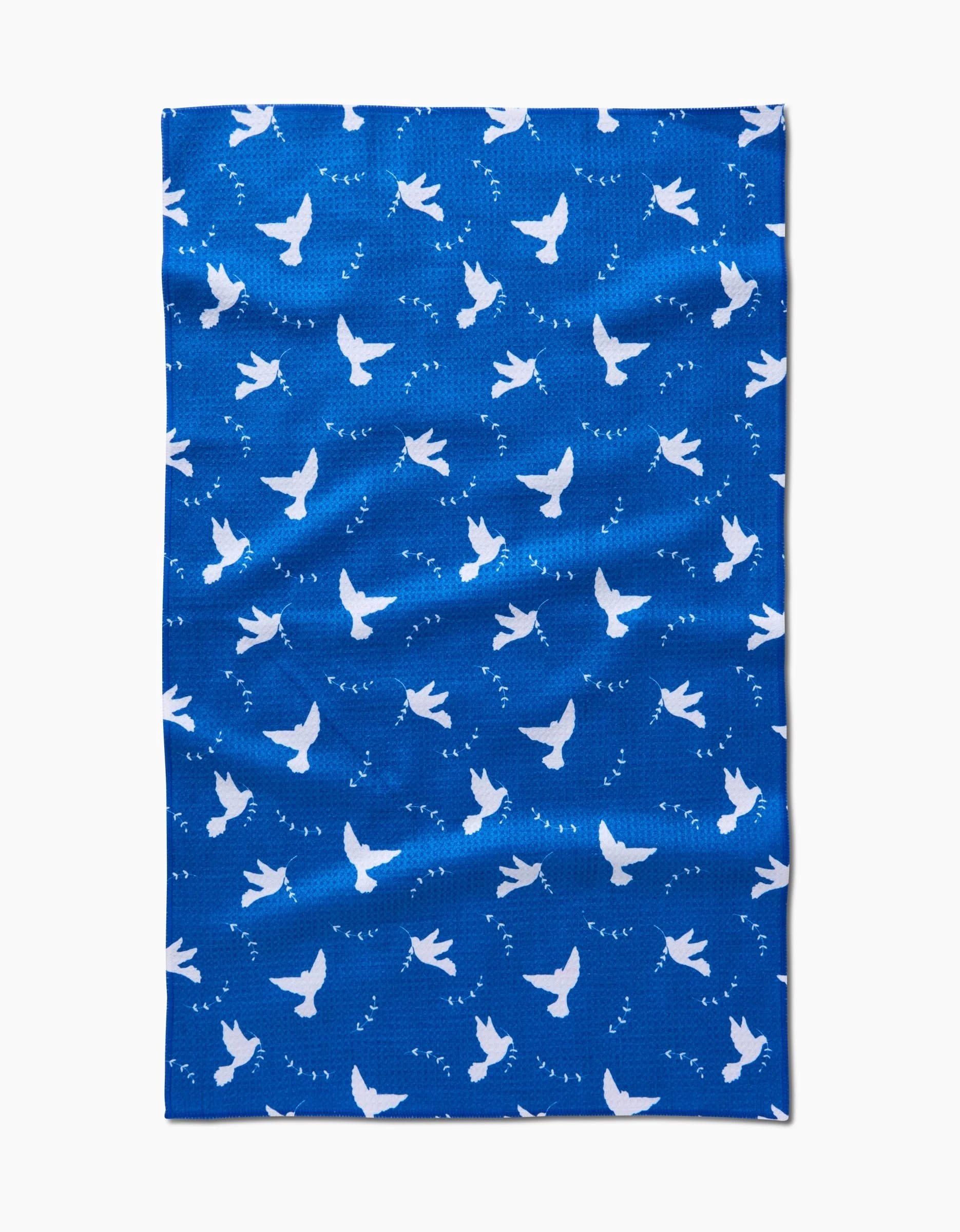 The Peace Dove kitchen tea towel by Pascale Dilger showcases a blue design with a repeating white dove pattern and scattered bird footprints, bringing charm and style to your space.