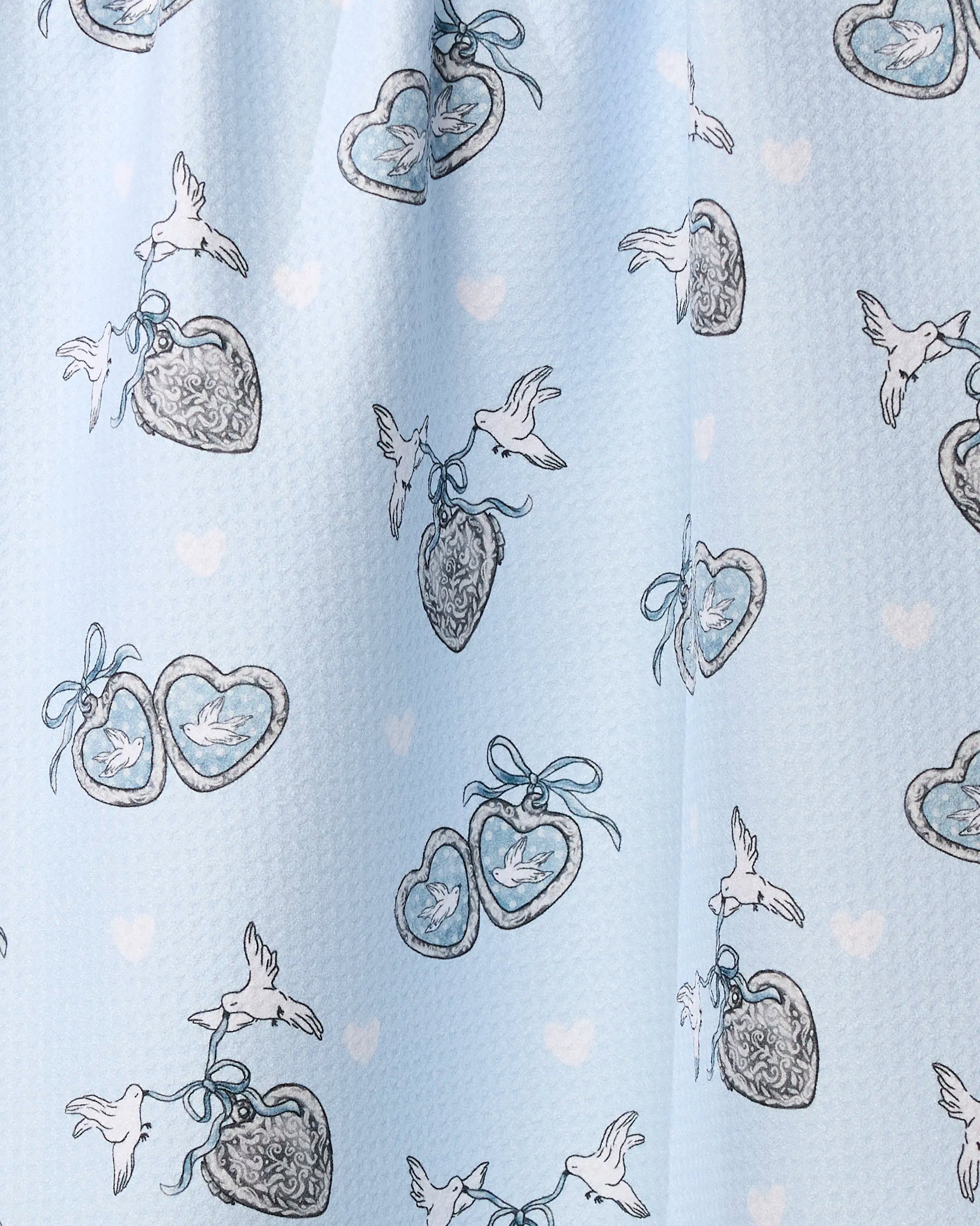 The Geometry Peace Doves tea towel features light blue recycled fabric with a white dove and heart locket pattern, accented by blue ribbons and scattered white hearts.