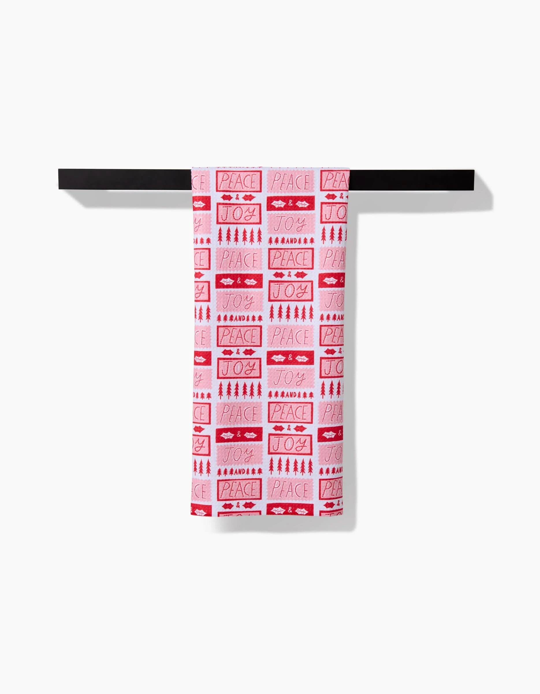 The Roxy Marj Peace Joy Stamps tea towel, with quick-dry fabric and red festive words like PEACE and JOY, hangs over a black rod against a plain white background.