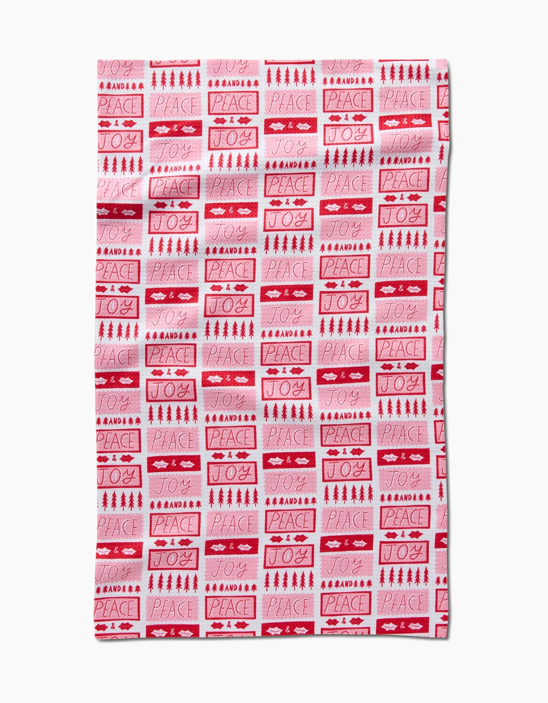 The Roxy Marj Peace Joy Stamps tea towel features a red and white holiday block pattern with words like Peace and Joy, plus festive symbols, all on recycled material with a white background.