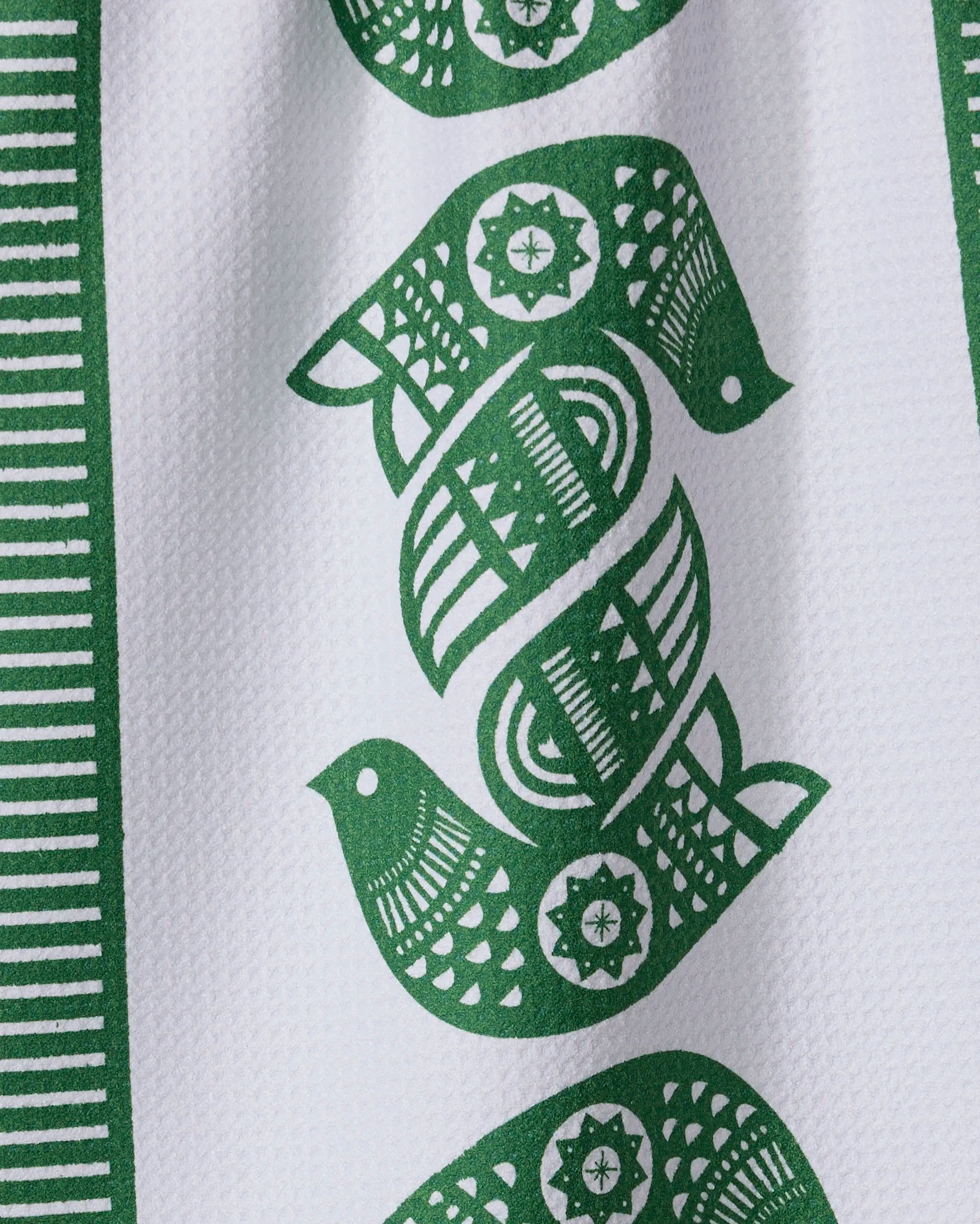 A close-up of the Geometry Peacebound recycled kitchen towel, showcasing green symmetrical bird and geometric patterns with vertical green stripes on the left edge.