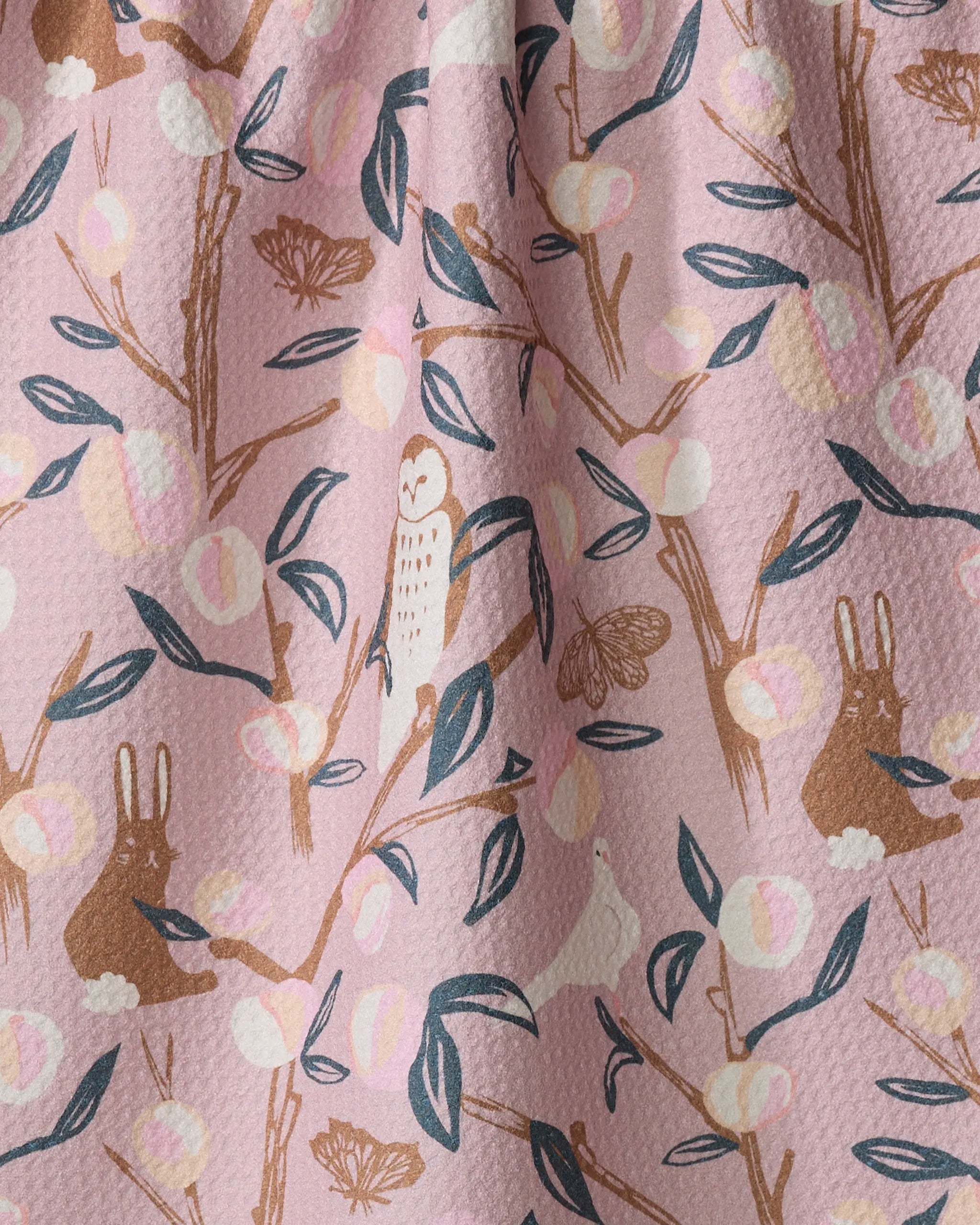The "Peach Tree" kitchen tea towel by Elisabeth Wing features brown rabbits, owls, moths, leafy branches, and pink, cream, and gold fruits on a light pink background—an eco-friendly way to brighten any space.