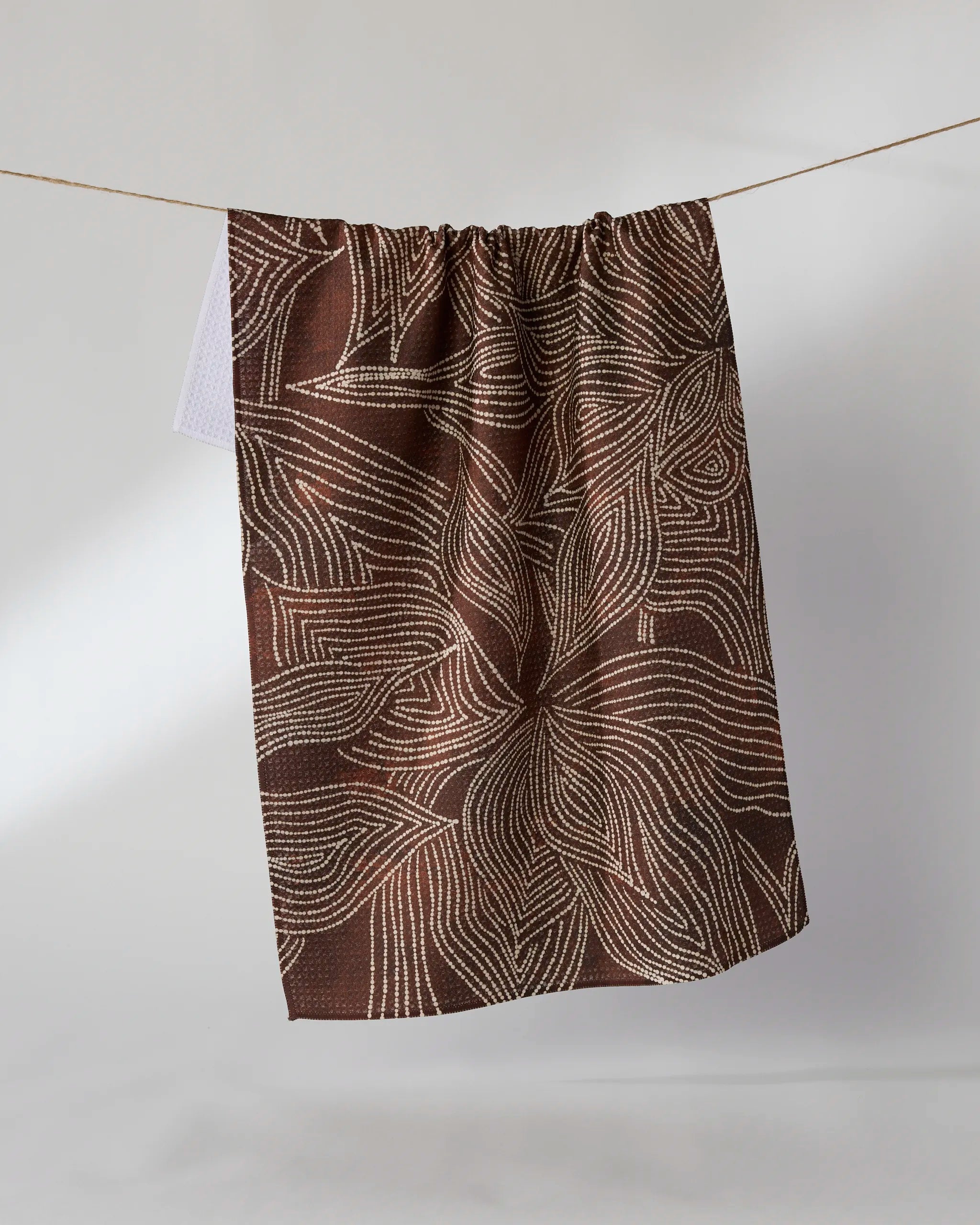 The Pearl Botanical tea towel by Geometry, featuring an abstract white stitched line pattern, hangs on a string against a plain light background.