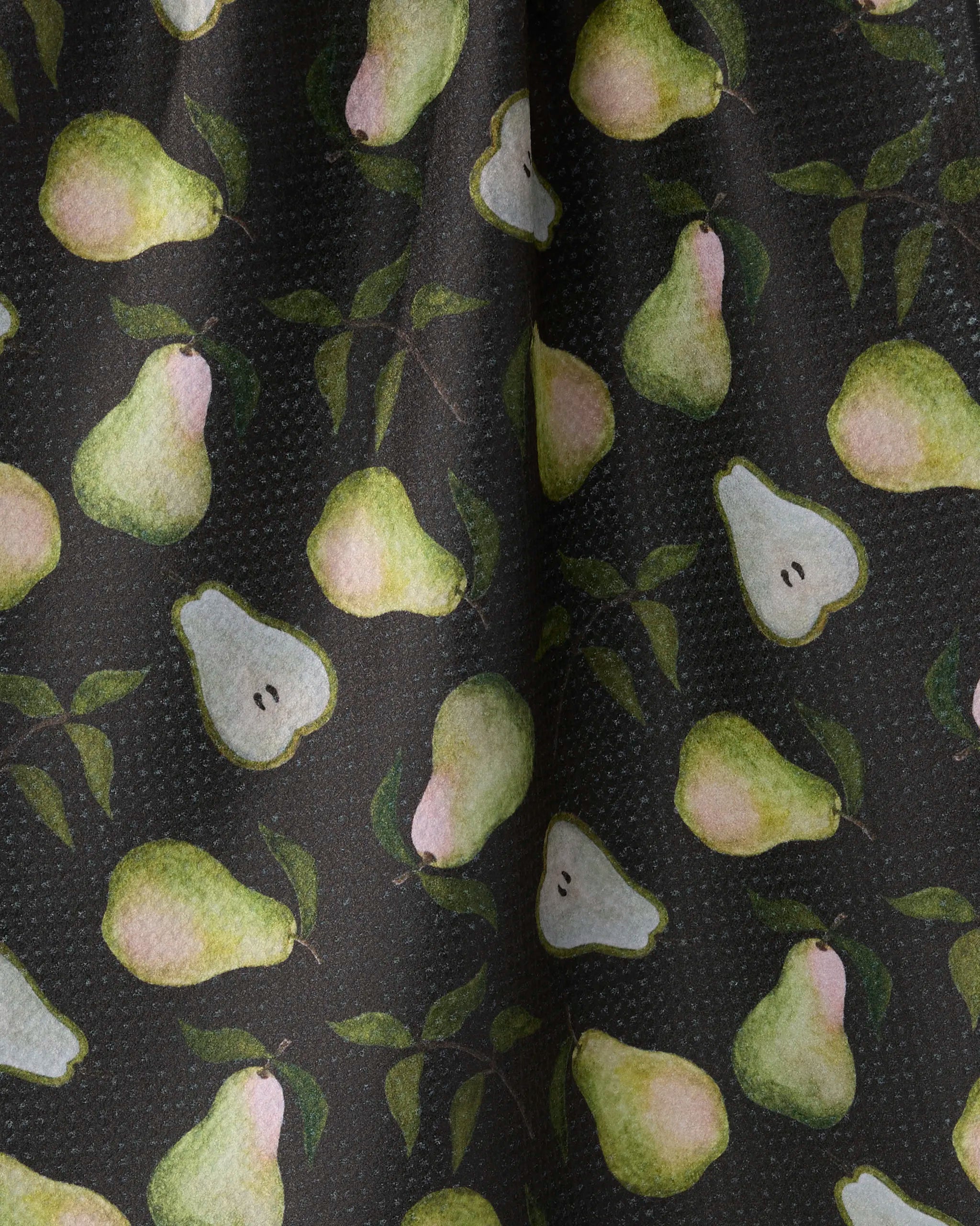 Pearwood by Geometry features a dark fabric with scattered whole and halved green pears, some with leaves—ideal for an eco-friendly tea towel to bring charm to your kitchen.
