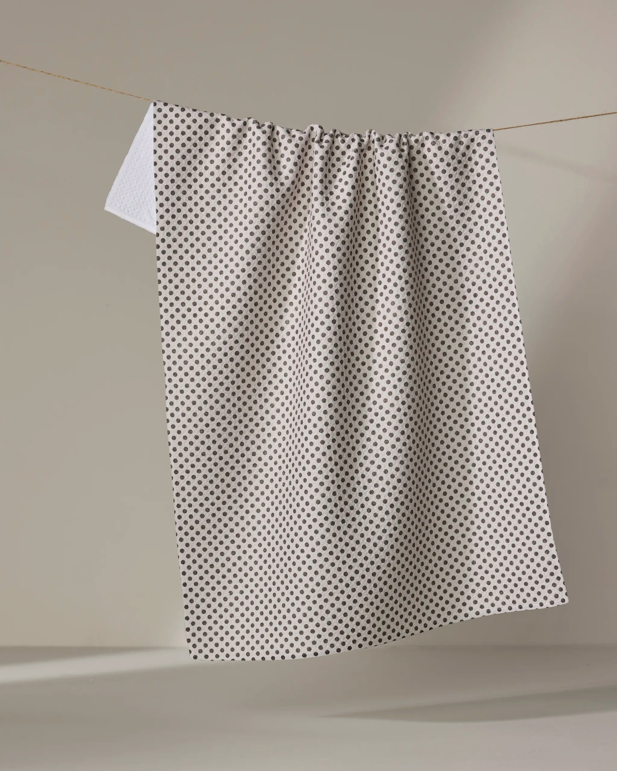 The Pebble kitchen tea towel by Jenny Keller features a pattern of small black dots on white and hangs from a clothesline against a light background. Made from recycled materials, it combines style with eco-friendly design.