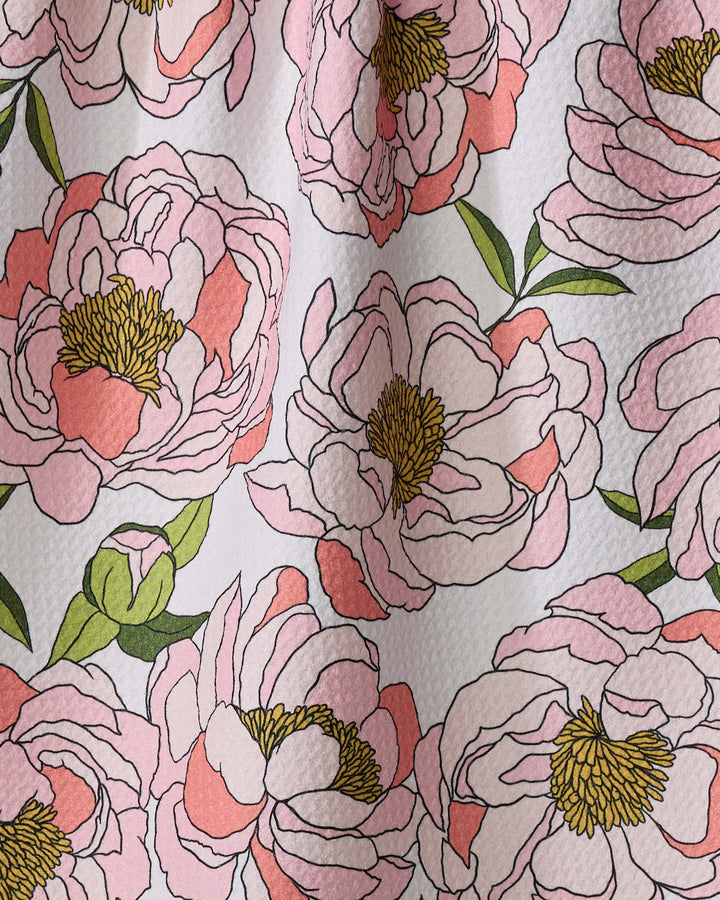 A close-up of Shelley Smith's Peony Paradise dish towel, featuring large pink peonies with yellow centers and green leaves on a textured white fabric—an absorbent and stylish way to brighten your kitchen.