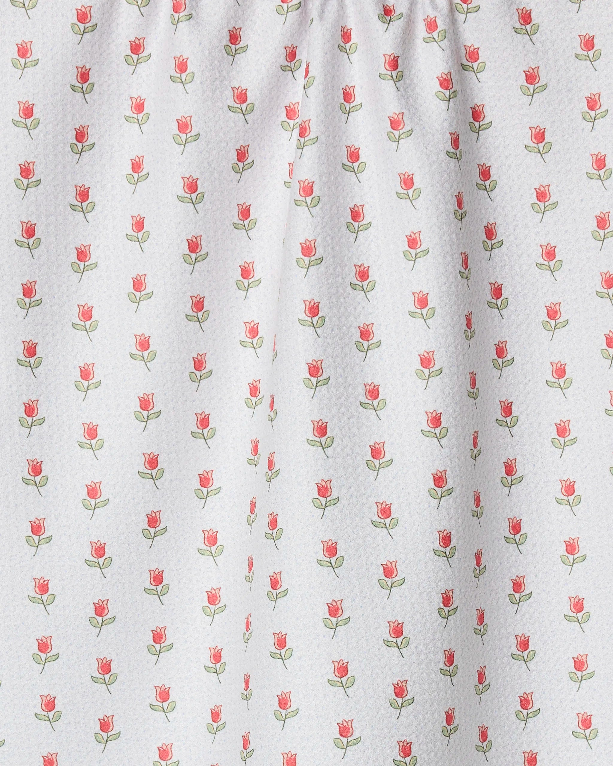 The Petite Tulip tea towel by Danelys Sidron features a white fabric with small red-pink tulip-like flowers and green leaves in neat vertical rows. Ultra-absorbent and slightly gathered at the top, it’s charming and functional.
