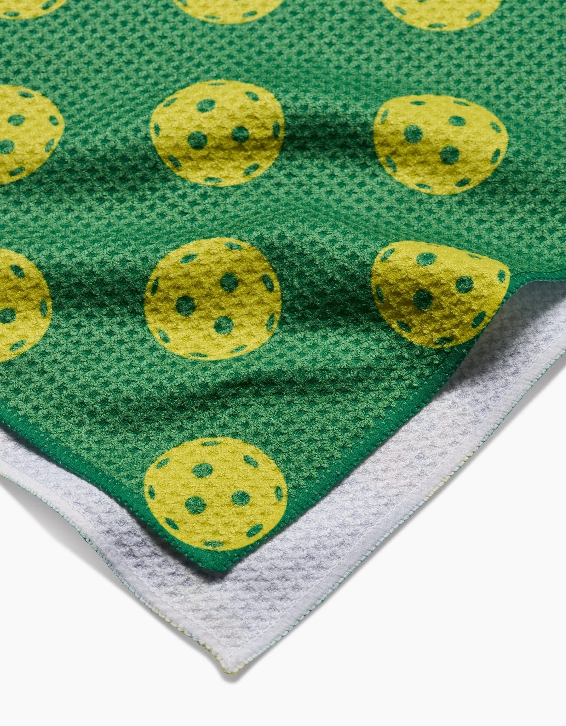 The GEOMETRY Pickleball Tea Towel features a textured green design with yellow circles and green dots, layered over a plain white towel, both made from soft Geoweave fabric.