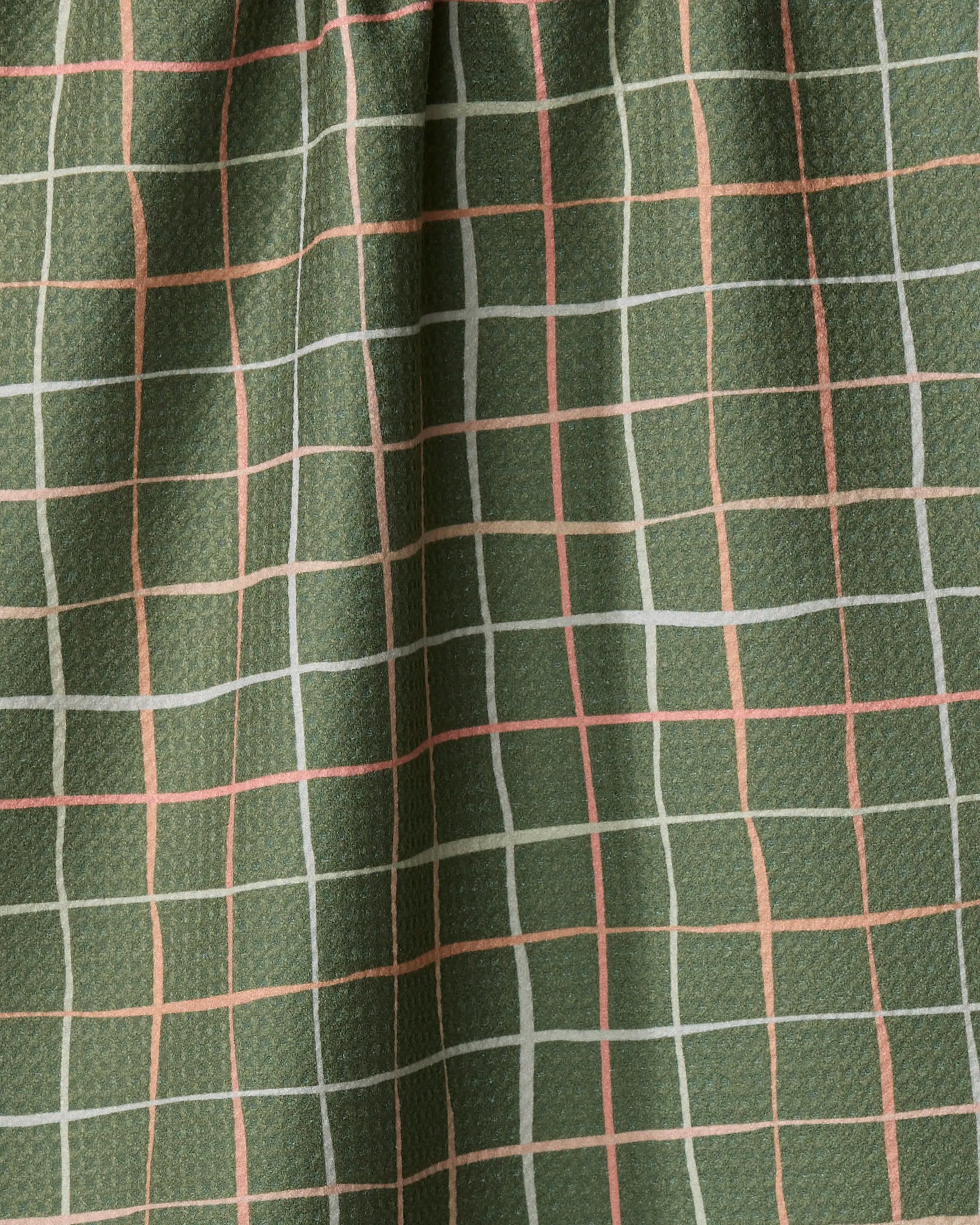 Close-up of Picnic tea towel by Anee Shah, featuring green textured fabric with a grid of white and peach lines. The draped folds highlight its recycled materials, making it an eco-friendly choice.