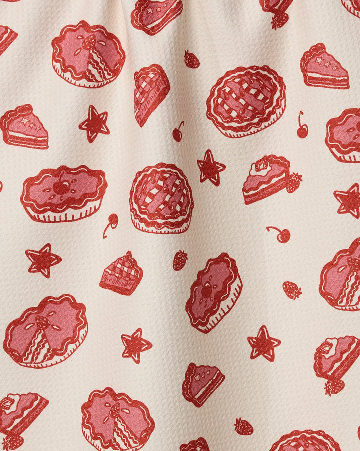 The Geometry Pie-triotic dish towel features playful, hand-drawn red pie illustrations, cherry slices, stars, and cherries on a cream background—perfect for adding charming absorbency and brightness to your kitchen.
