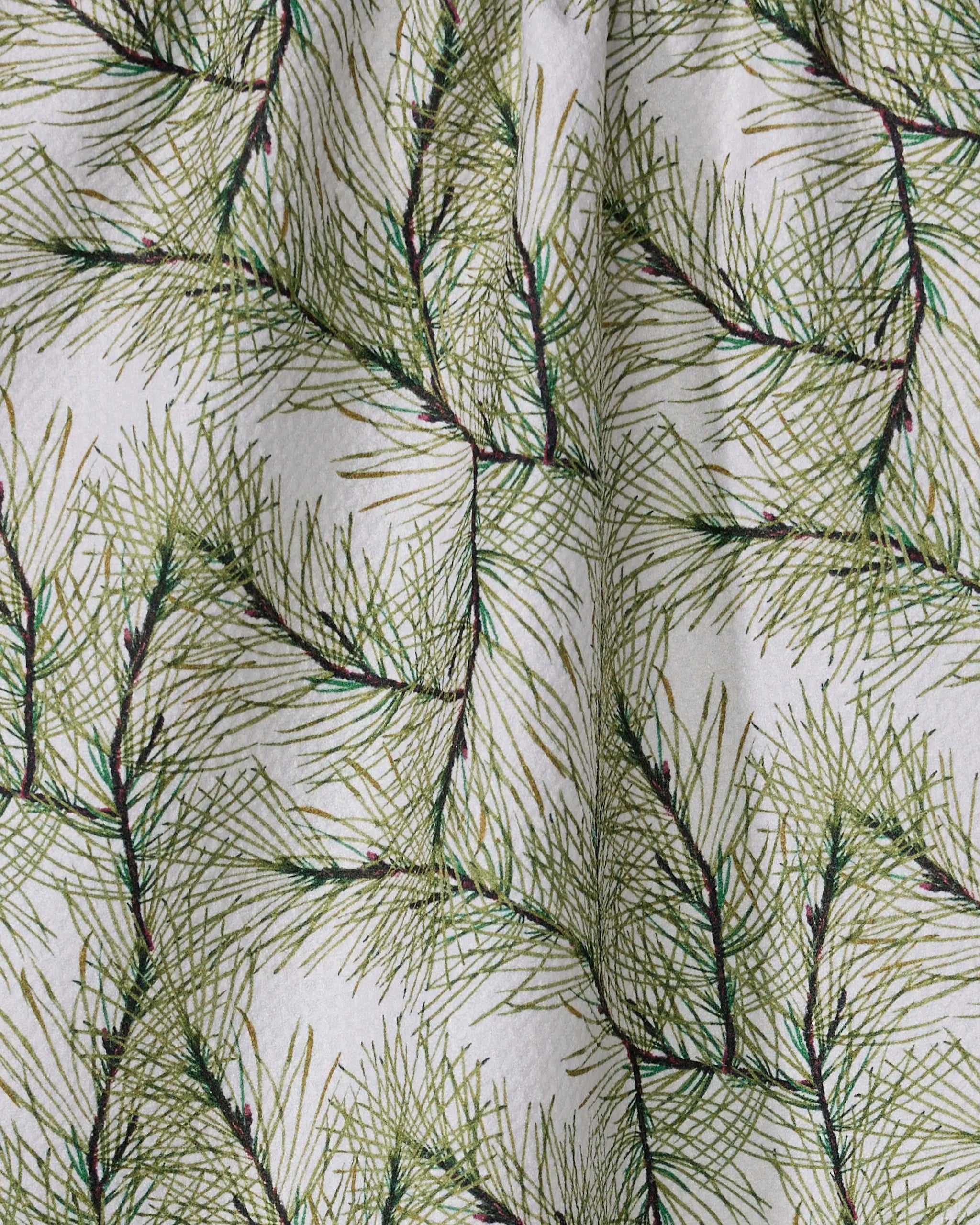 A close-up of Geometry's Pinewell towel showcases its ultra-absorbent fabric, featuring a festive pattern of overlapping green pine needles on a white background with gentle folds for a natural look.