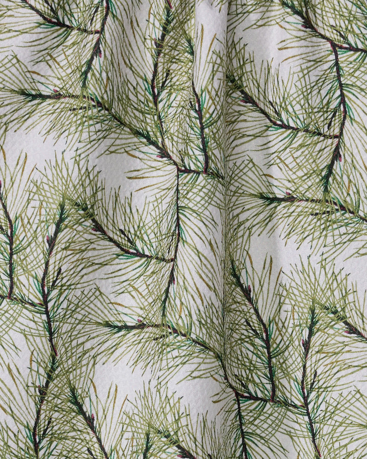 A close-up of Geometry's Pinewell towel showcases its ultra-absorbent fabric, featuring a festive pattern of overlapping green pine needles on a white background with gentle folds for a natural look.