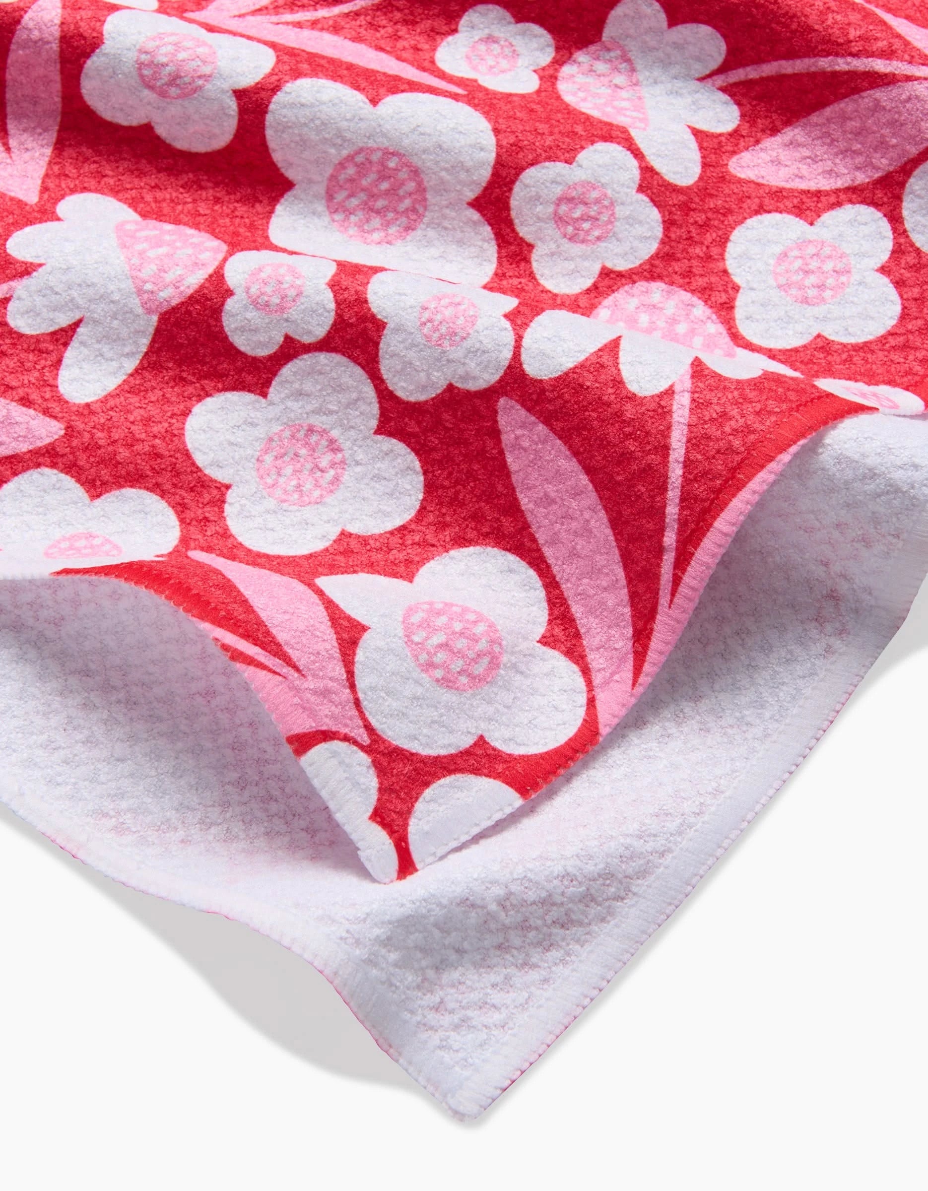 A close-up of the Pink Blooms ultra-absorbent towel by Charlie Rowan Designs, showcasing its pink and white floral pattern with a folded corner highlighting the soft, textured white underside.