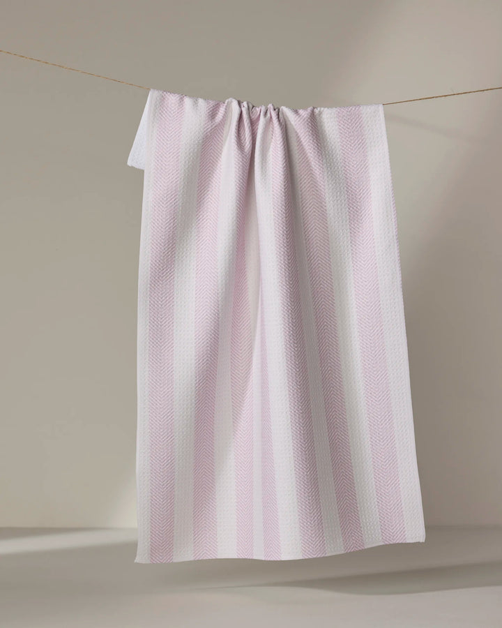 The Teri the Butter Pink Chevron Stripe ultra-absorbent towel hangs on a clothesline against a neutral beige background.