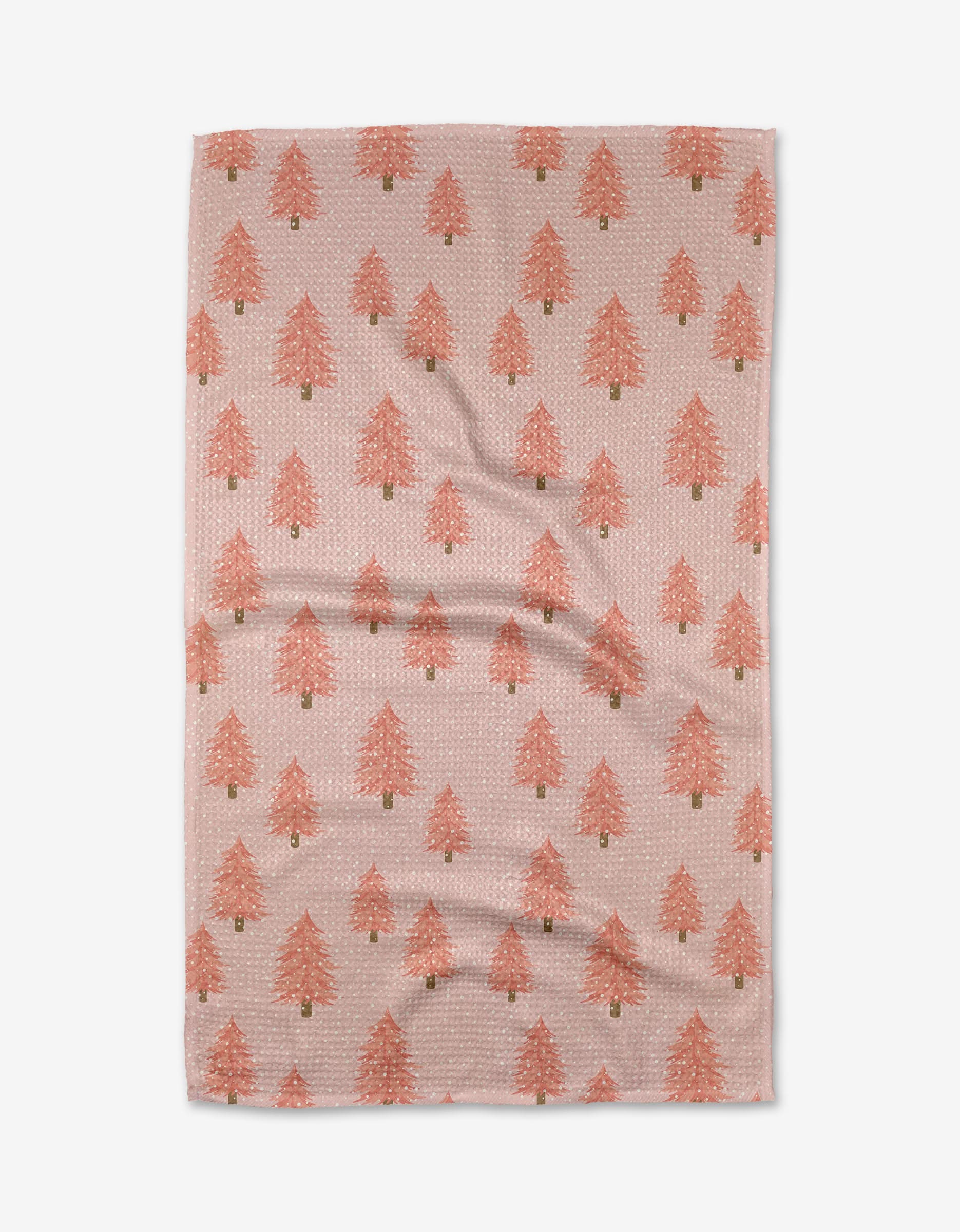 The Pink Christmas tea towel by Megan Kampa features a light pink background with red Christmas trees and white dots in neat rows on a quick-drying surface.
