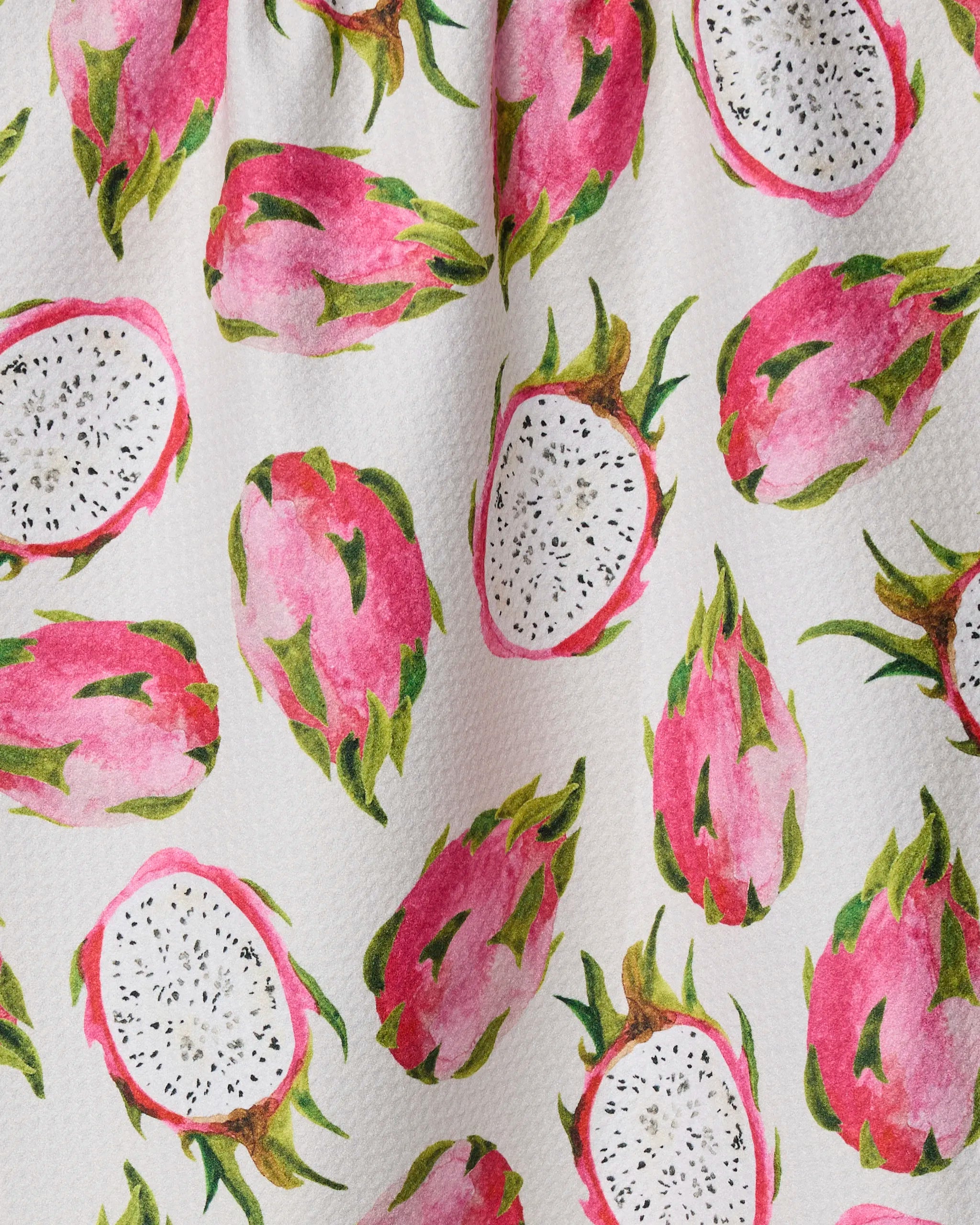 Geometry’s Pink Dragon fabric showcases whole and halved pink dragon fruits with green leaves on a textured white background—ideal for a vibrant, eco-friendly tea towel or kitchen towel made from recycled materials.