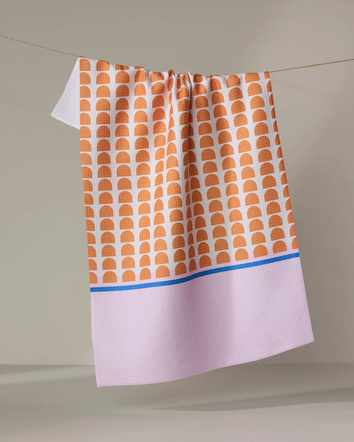 Pink Illusion by Happy Hemera is an ultra-absorbent tea towel featuring orange semi-circles on white, a blue stripe, and a light pink section—perfect for adding color to your kitchen.
