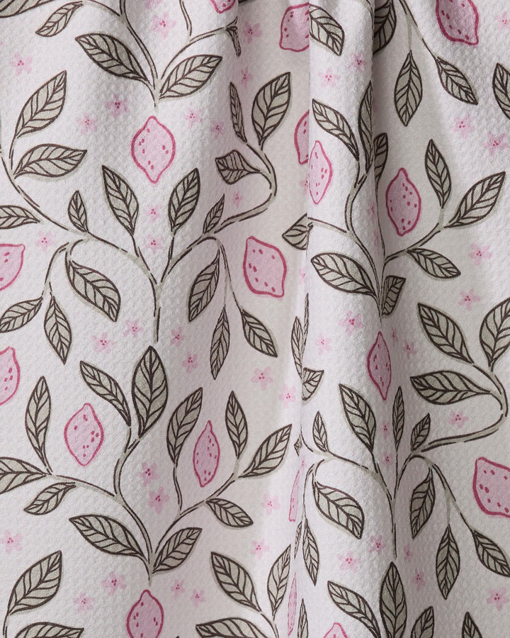 The Pink Summer Lemons tea towel by Teri the Butter features a white fabric with brown leafy branches, pink lemons, and small pink dots. Made from recycled materials, it has soft folds and a subtly textured surface.