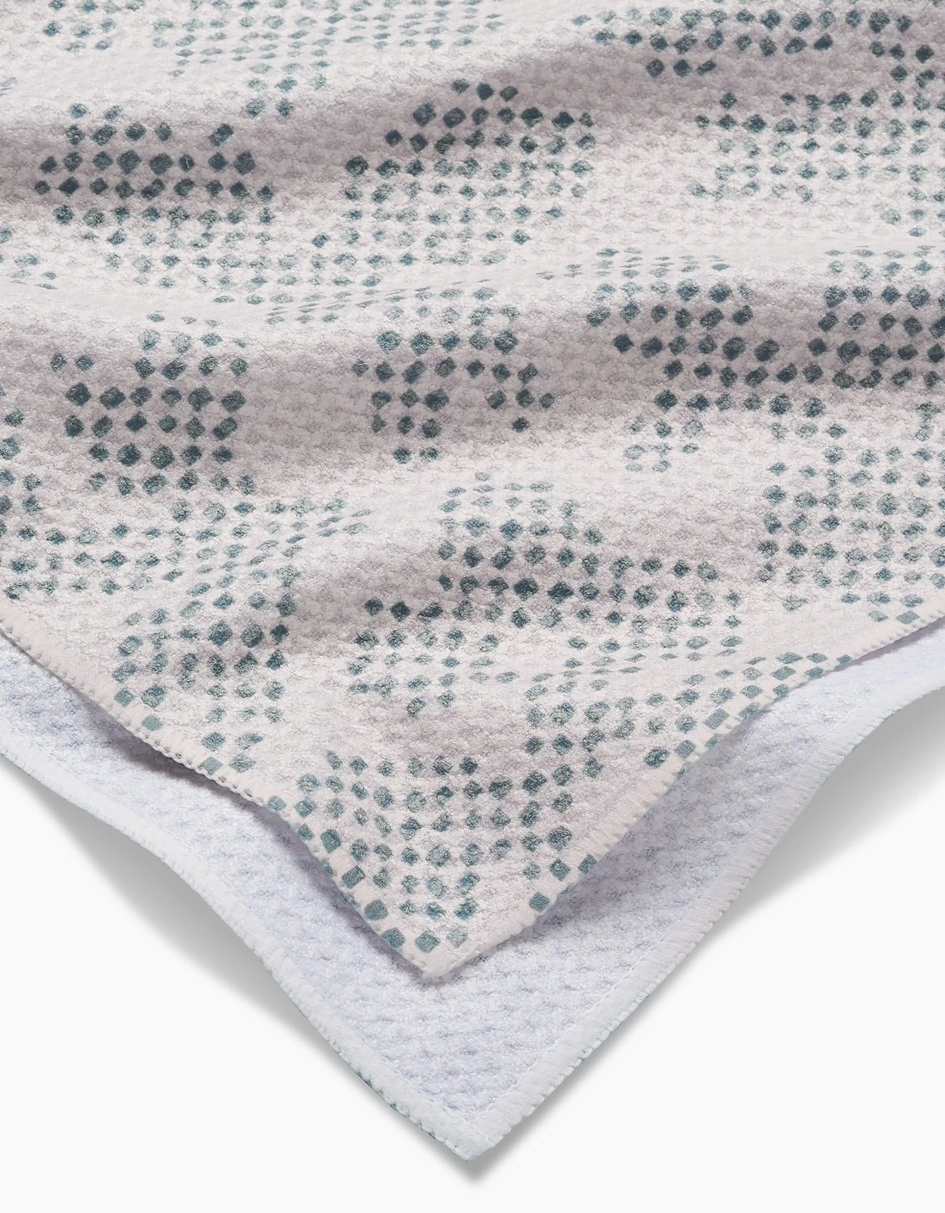 A close-up of Studio Jeannot’s Pixie Sage tea towel shows soft, textured Geoweave™ fabric with blue-green dots on a light background. Layered edges and a subtle weave are crafted from recycled materials.
