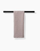 A Plated Fall Berry Natural tea towel by Hufton Studio, featuring a patterned brown and white geometric design, is neatly draped over a black bar against a plain white background.