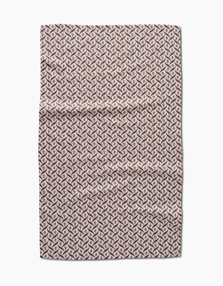 The Hufton Studio Plated Fall Berry Natural tea towel features a repeating geometric pattern in brown, tan, and white that creates a 3D cube effect. Made from Geoweave fabric, the towel is shown flat on a white background with visible creases.