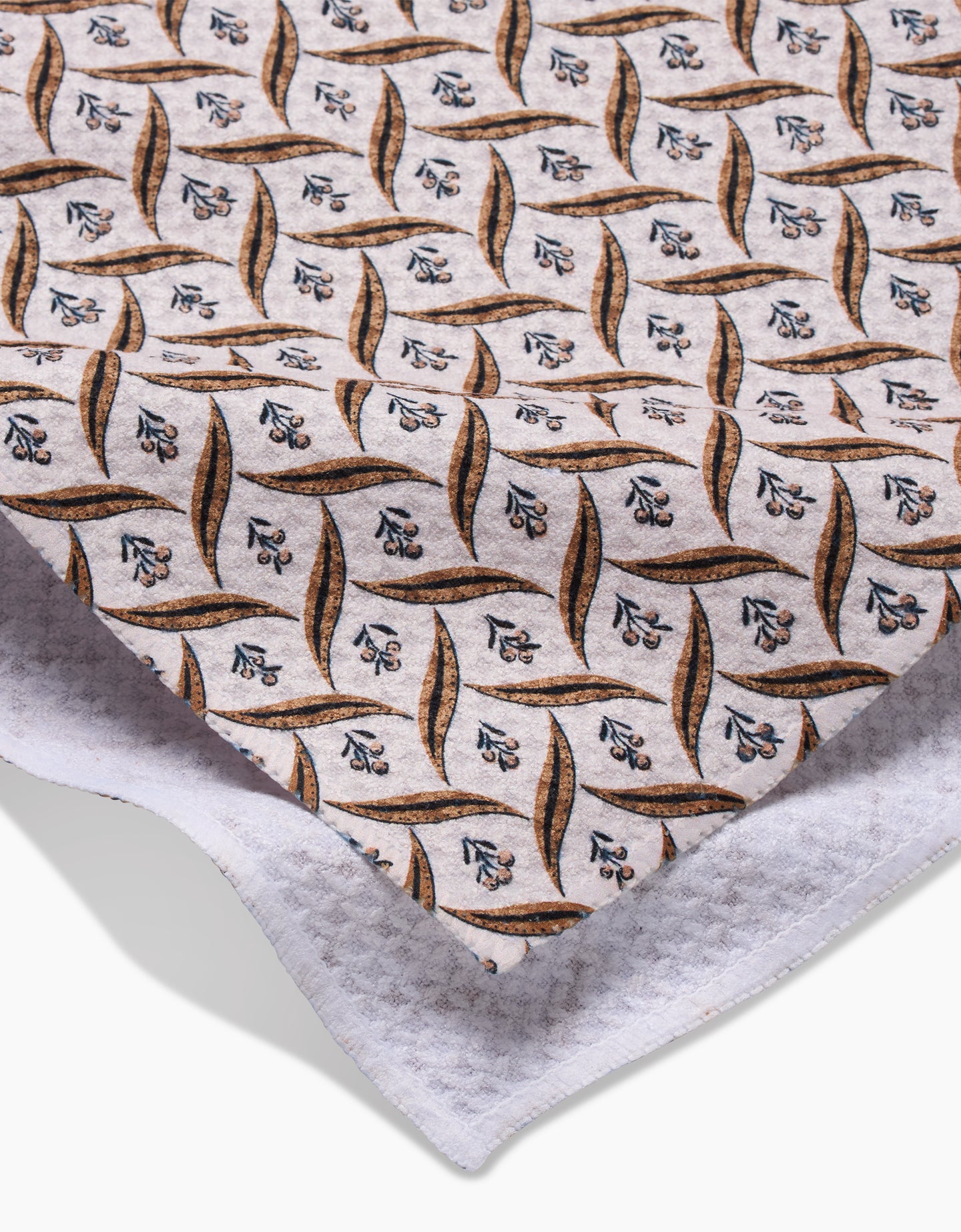A close-up of Hufton Studios Plated Fall Berry Natural fabric, featuring a repeating leaf and floral design in brown, blue, and black on white, made from recycled materials and layered over textured white cloth.