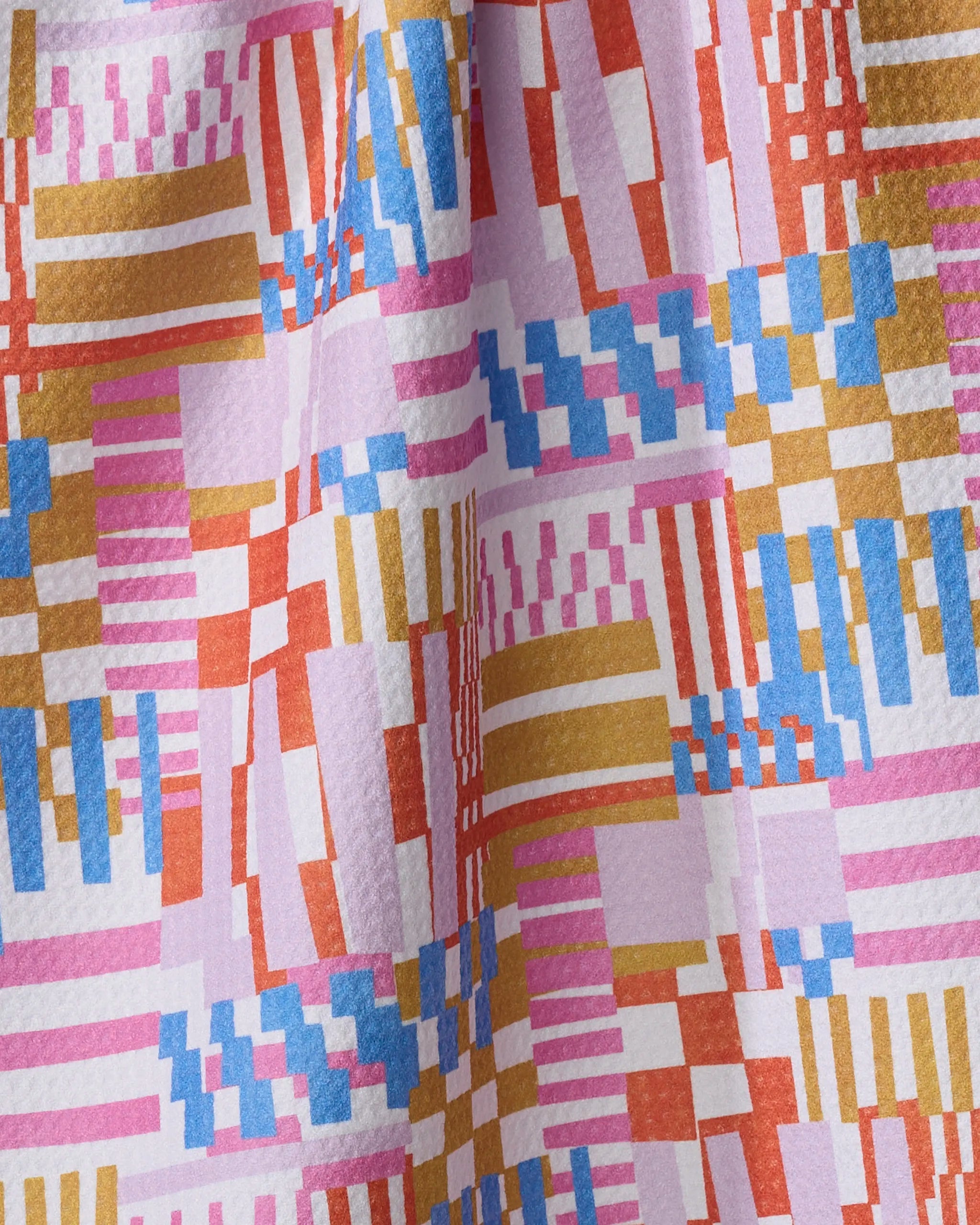 A close-up of the Playful Stripes quick-drying towel by Claire Iglesias, showcasing its geometric pattern in pink, blue, gold, orange, and white with subtle texture and gentle draping.