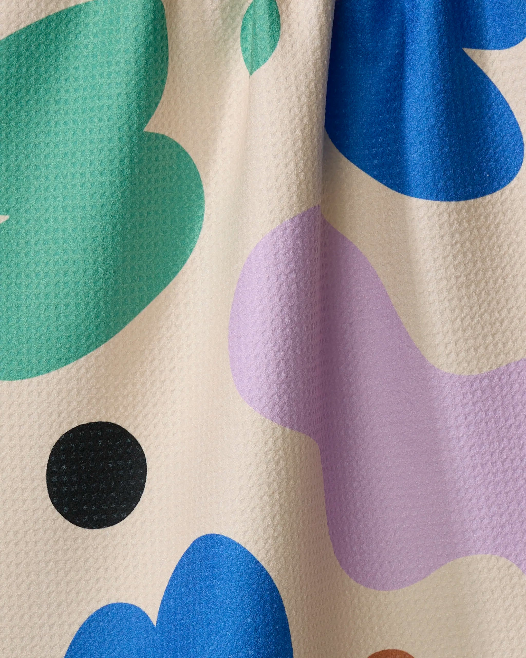 A close-up of Playground fabric by Beetle Ink Co., showing large abstract shapes in green, blue, purple, black, and brown on a cream background. The textured material is softly draped and may be made from recycled kitchen towels.