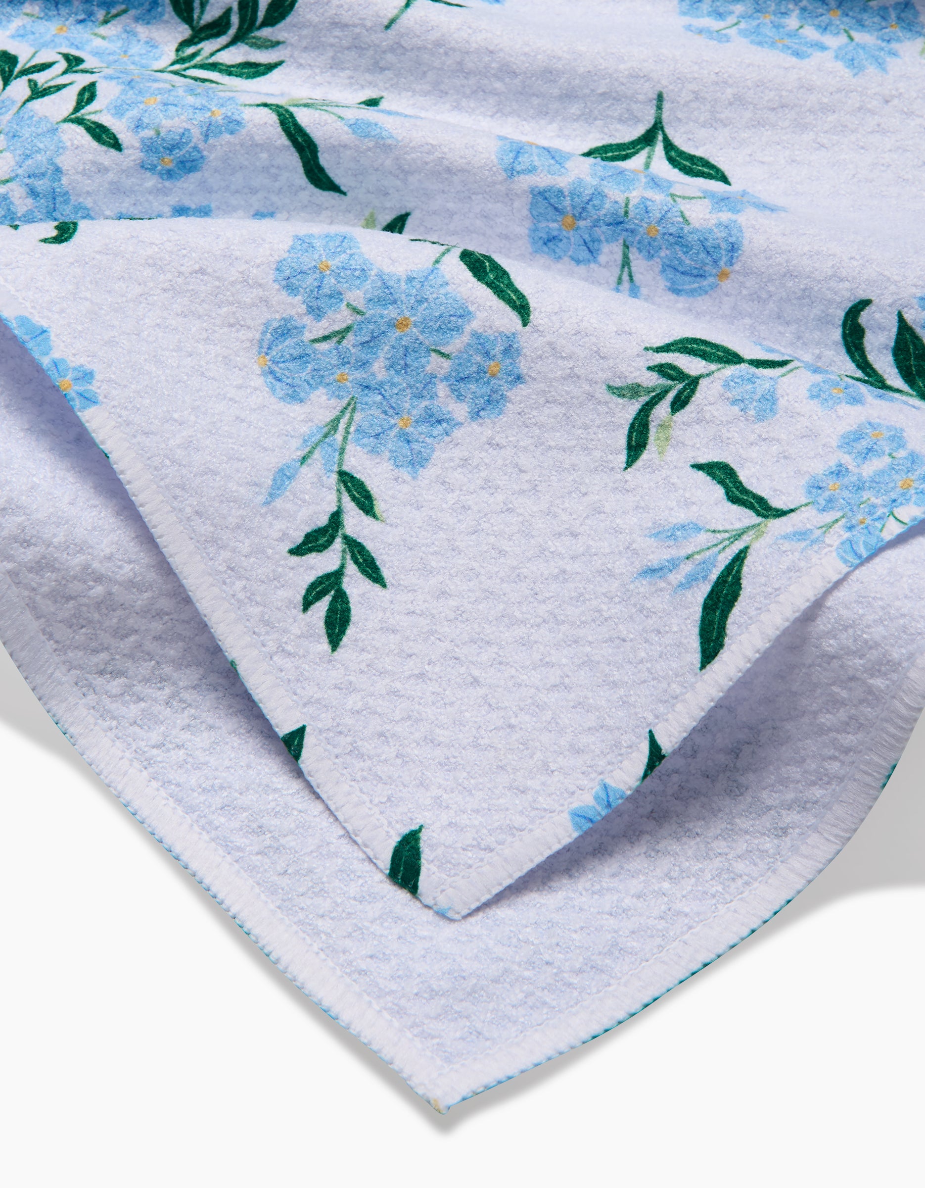 A close-up of the Danelys Sidron Plumbago towel, featuring a soft white Geoweave™ fabric with a light blue floral and green leaf design, neatly folded to showcase its ultra-absorbent thickness and printed details.