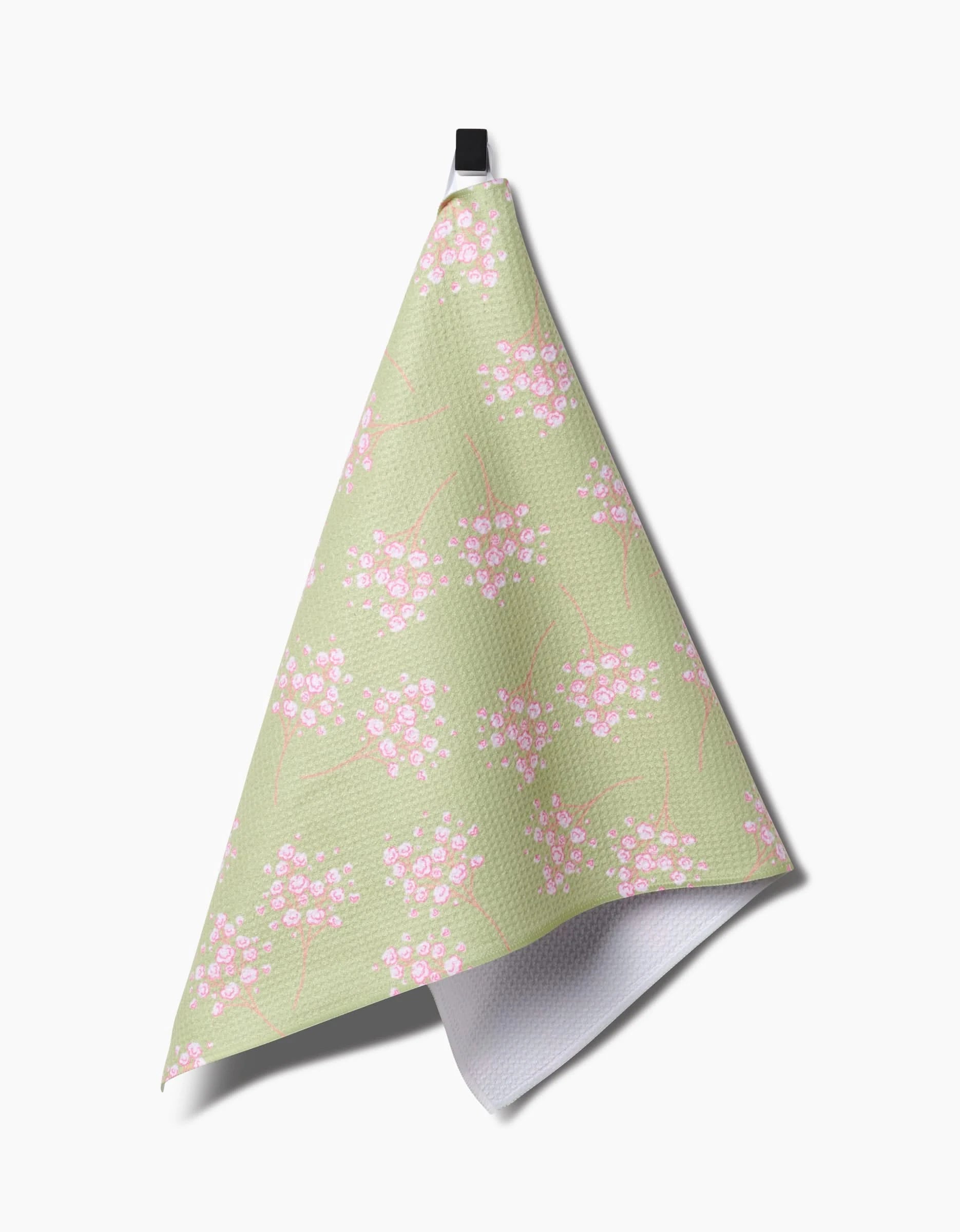 The Sarah Reed Pocket of Posies kitchen towel, crafted from ultra-absorbent Geoweave fabric and adorned with small pink and white flowers, hangs by a black loop against a white background.
