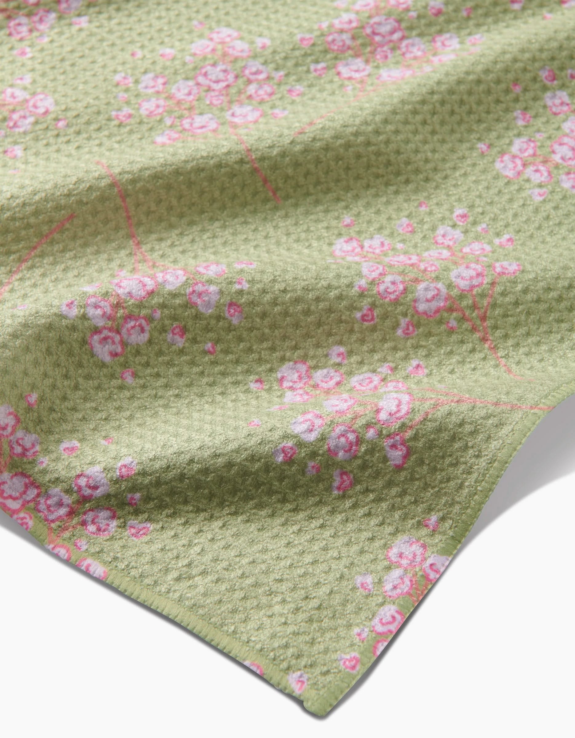 A close-up of Sarah Reed’s Pocket of Posies shows textured green Geoweave fabric with pink and white cherry blossom branches, a waffle-like ultra-absorbent surface, and neatly finished edges.