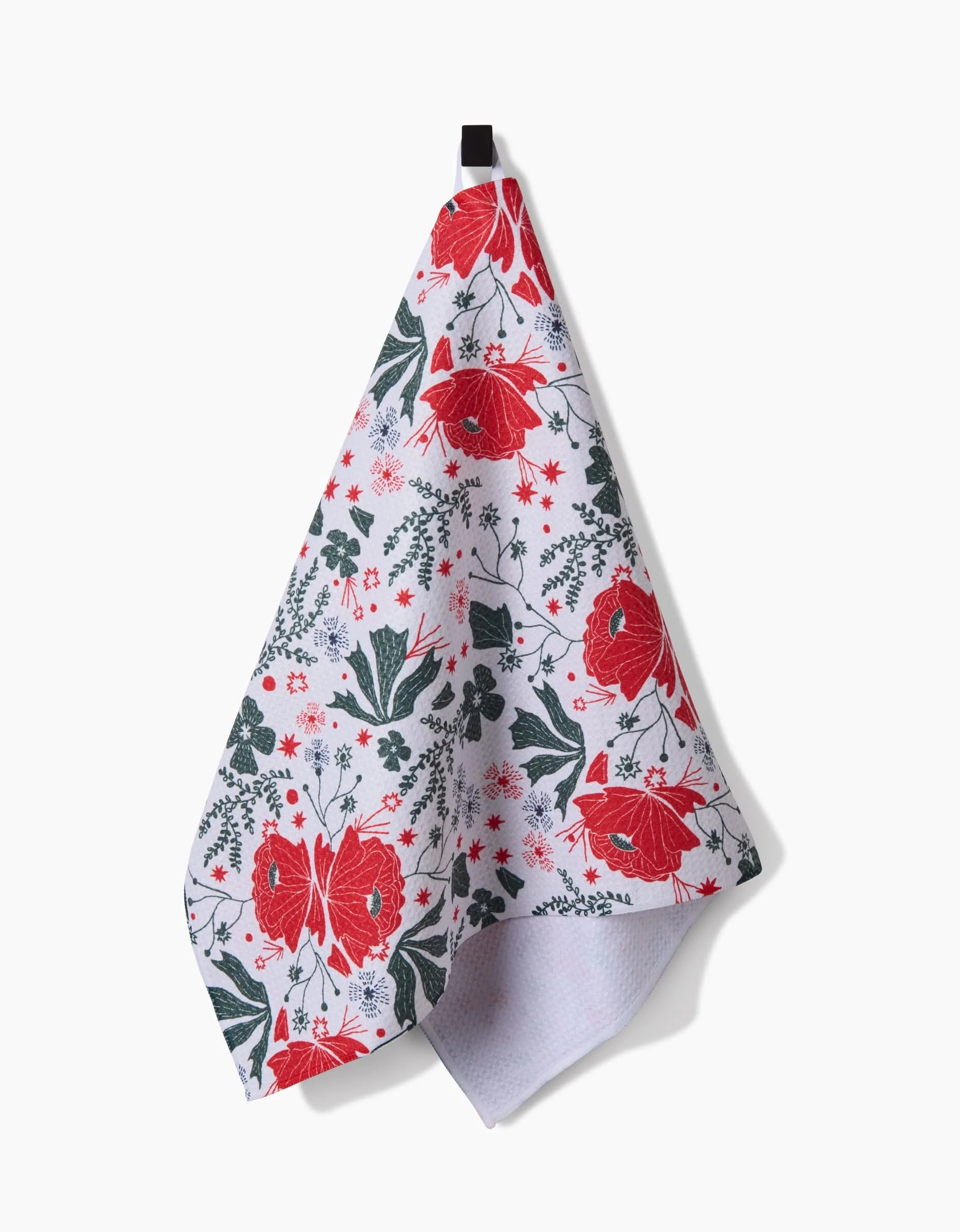 The Ash Cascade Poinsettia Bramble tea towel features large red flowers, green leaves, and red-green accents on Geoweave fabric. It hangs from a black loop against a plain white background.