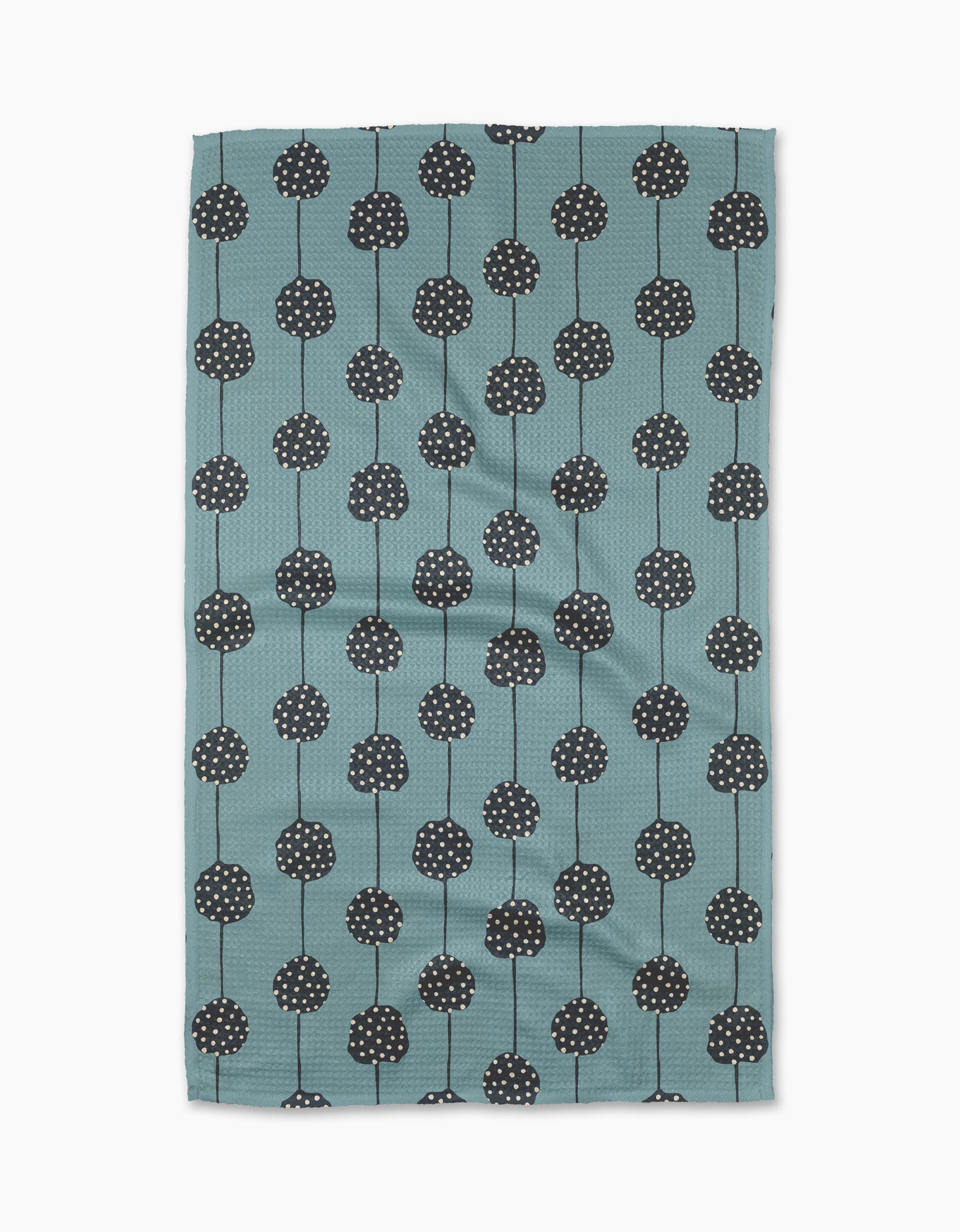 The Polka Dot Garland tea towel by Lizzie Clark is made from recycled materials in teal, with a pattern of black round flowers with white dots and thin stems arranged in vertical rows. The slightly wrinkled fabric is displayed on a white background.