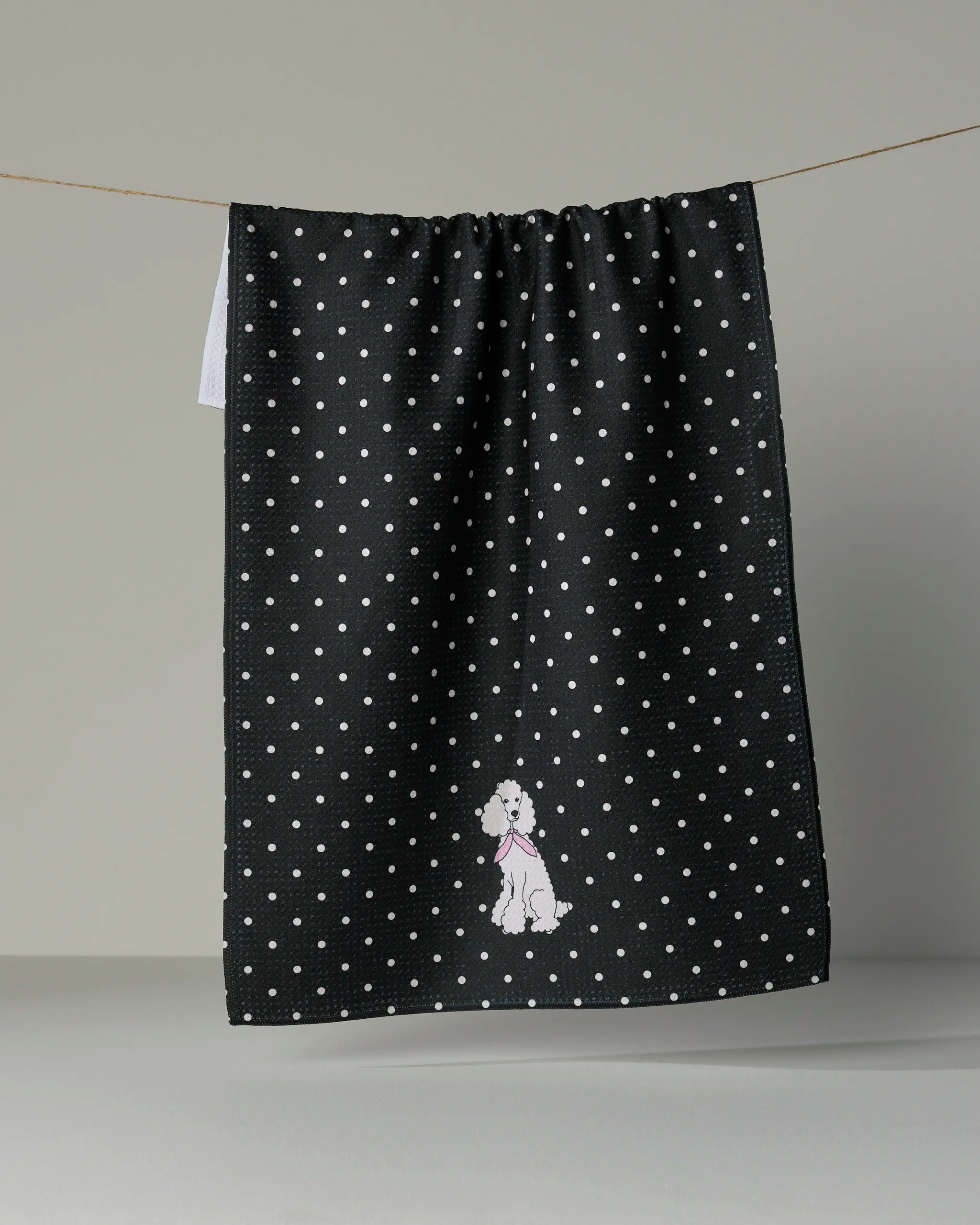 The Geometry Poodle Charm tea towel features a sleek black design adorned with playful white polka dots and is finished with a small embroidered white poodle donning a pink scarf at the bottom. Ultra-absorbent, stylish, and practical, it’s the perfect accent for any kitchen.