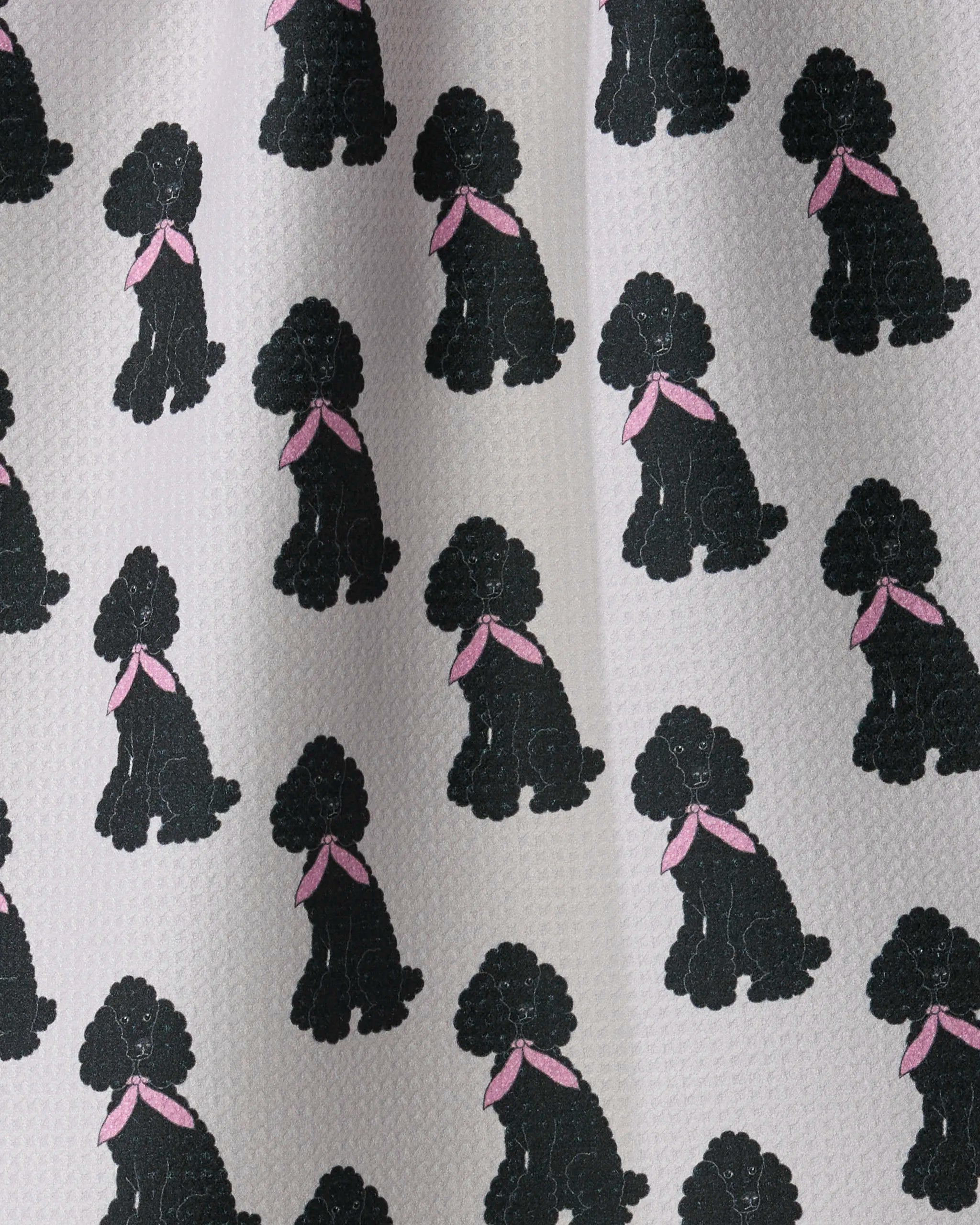 Add playful elegance to your kitchen décor with the Poodle Parade recycled tea towel from Geometry. This towel features a light background adorned with repeating illustrations of black poodles wearing pink bows, while its visible recycled texture offers both style and sustainability.