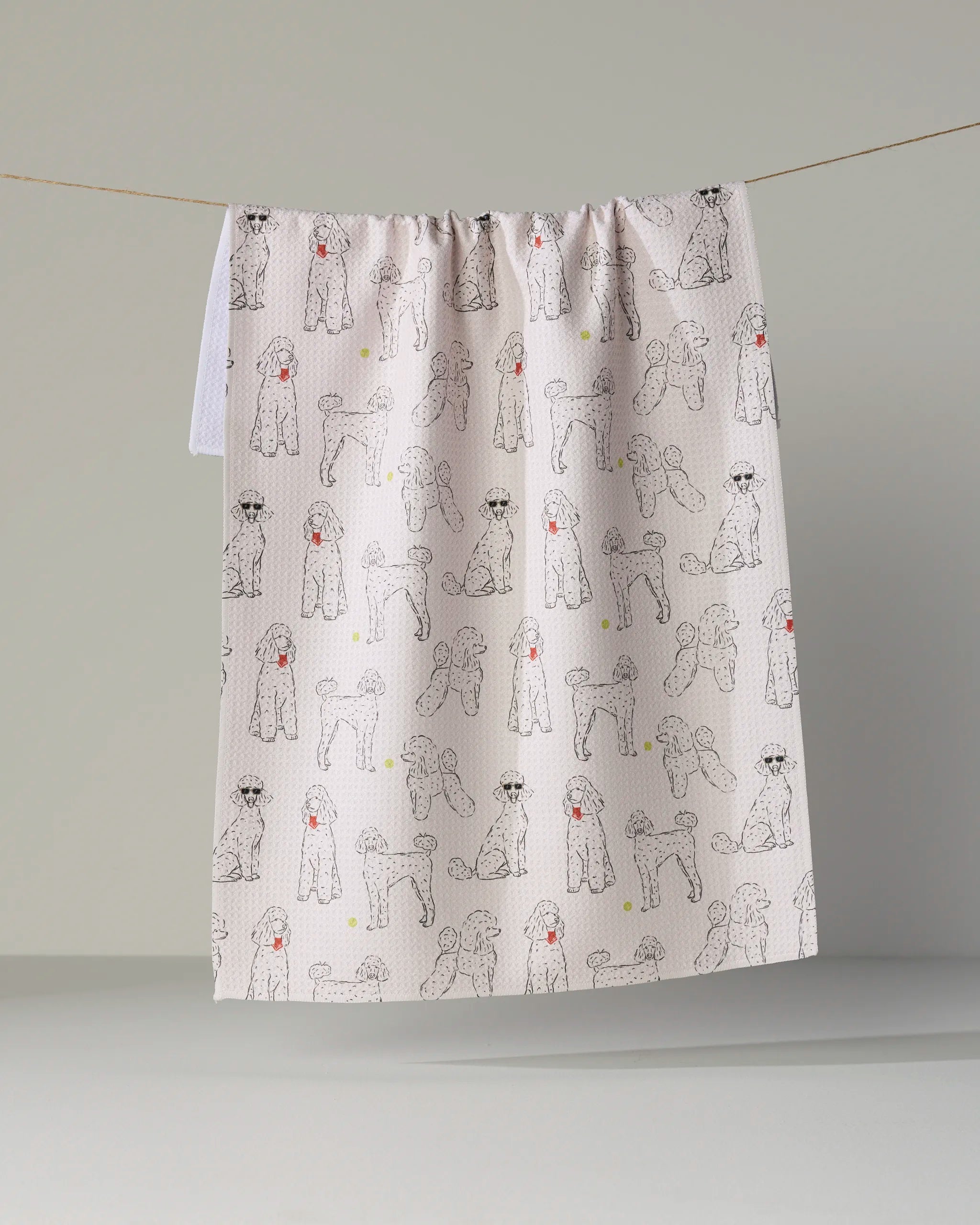 Introducing “Poodle Party” by Geometry—a delightful kitchen tea towel showcasing an array of black and white poodles, some adorned with cheerful red accents, playfully hanging on a string against a clean, simple backdrop. Both stylish and highly absorbent, this dish towel adds personality to your kitchen while making everyday cleanup effortless.