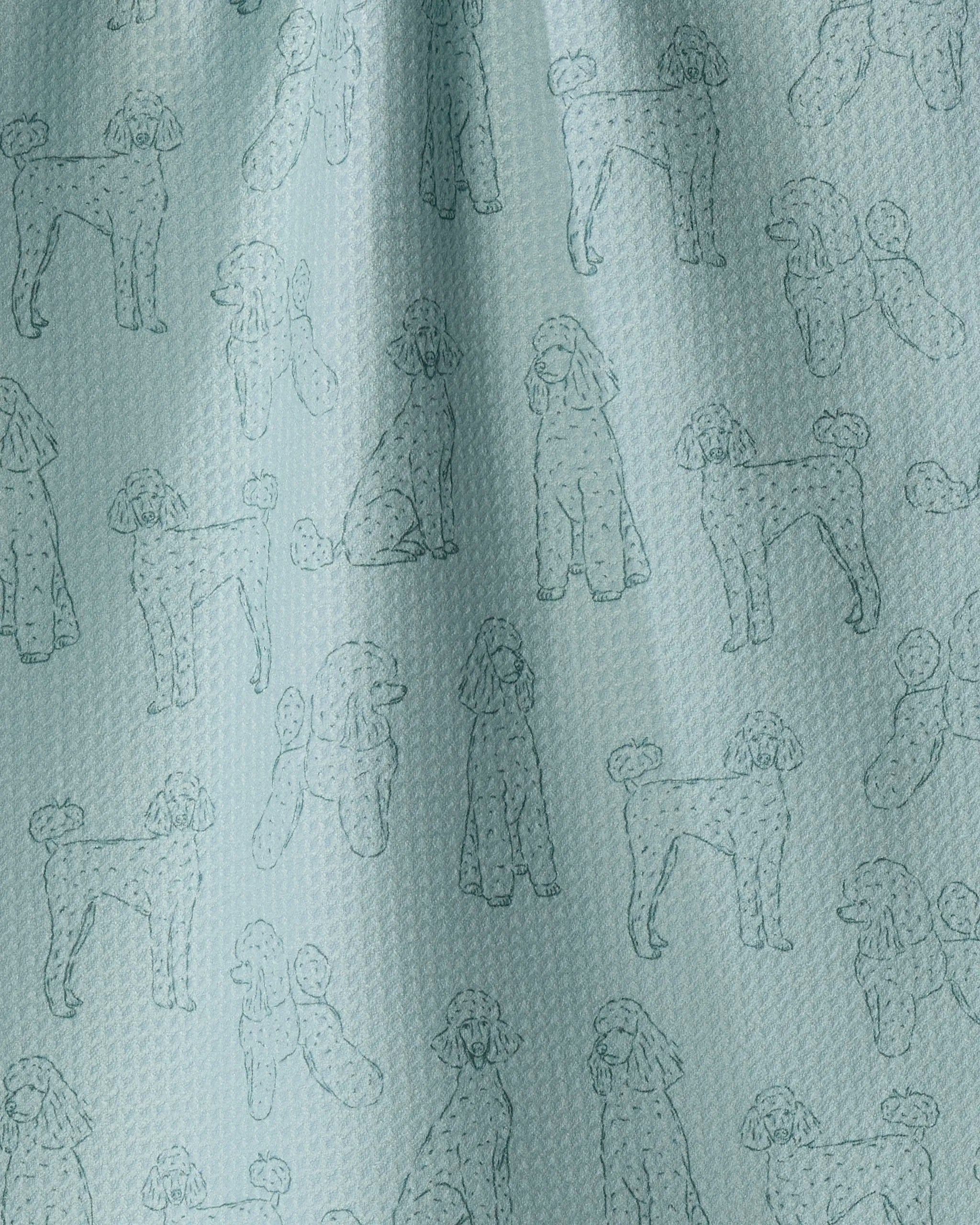 The “Poodle Pups” dish towel from Geometry features a light blue, textured fabric adorned with simple line drawings of poodles in playful poses repeating across the surface, offering both charm and absorbency for your kitchen.