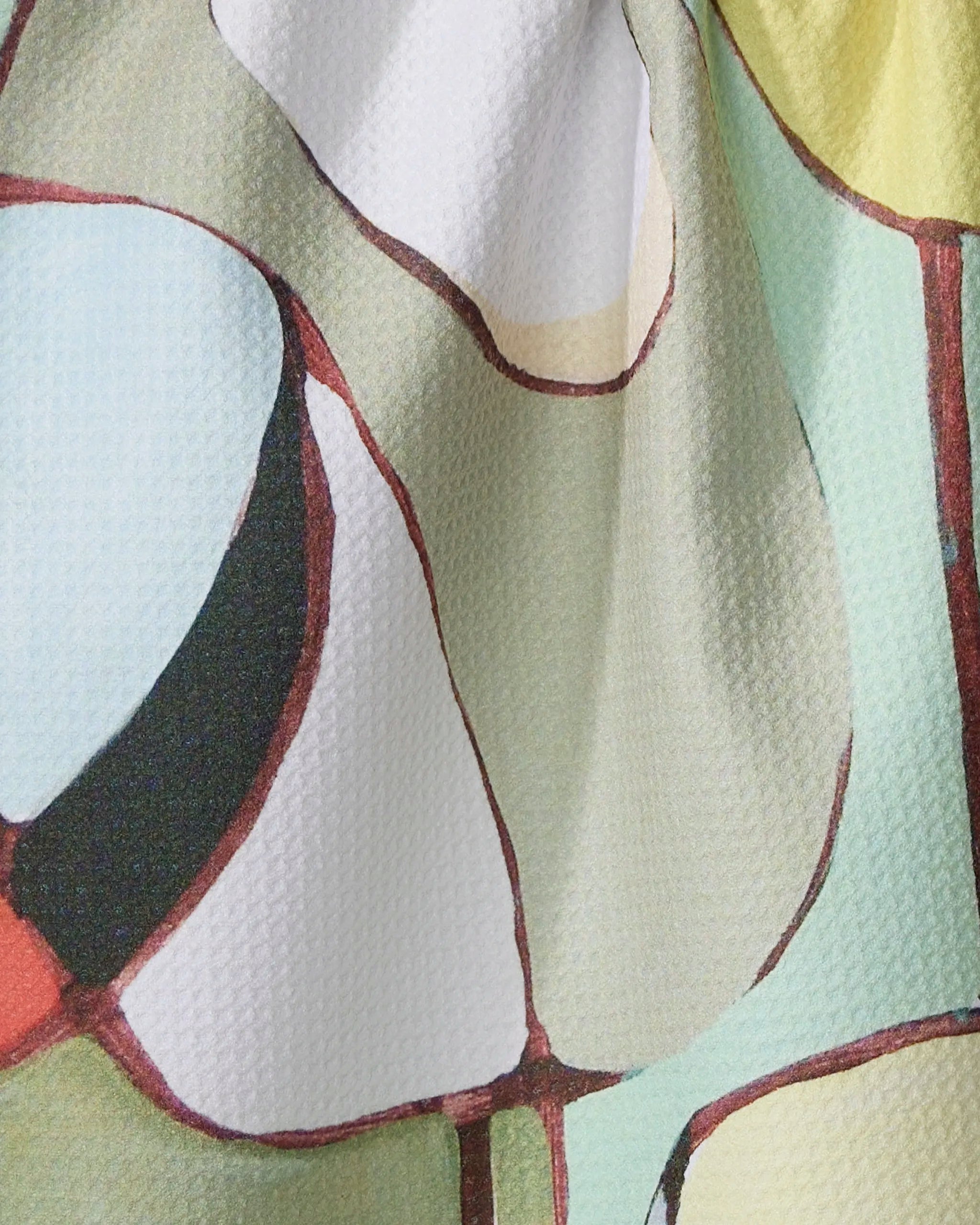 The “Poppies on Mint” tea towel by Rachel Austin features an abstract, multicolored pattern in pale green, white, black, red, and beige. Made from recycled materials, it’s quick-drying and adorned with curved, interconnected shapes for visual interest.