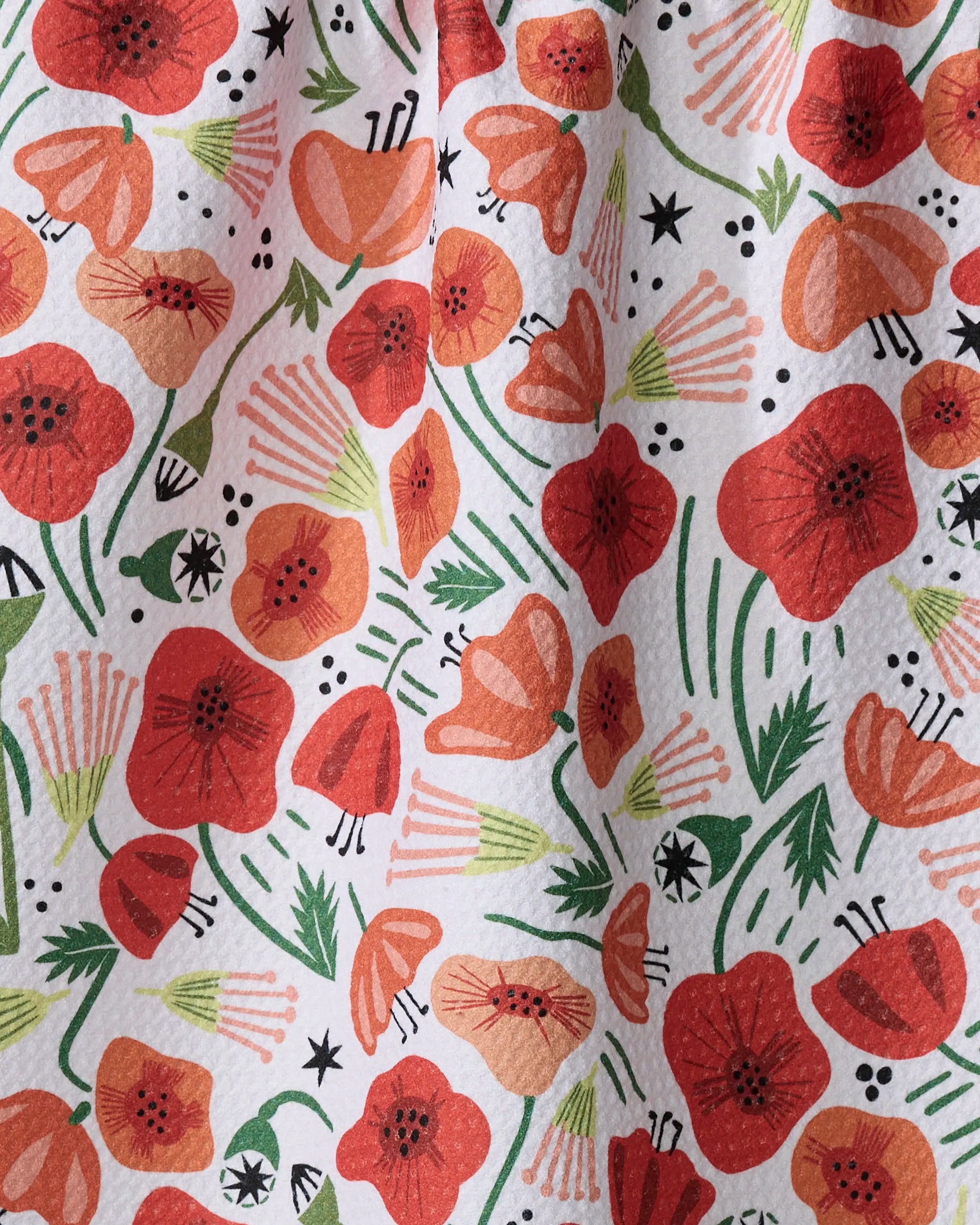 Elisabeth Wing’s “Poppy Power” recycled kitchen towel features a repeating pattern of red and orange poppies, green leaves, and black accents on white for a vibrant, lively look.