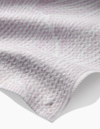 A close-up of the Geometry Posh Petals Blushed Bergamot kitchen towel, featuring a soft, textured design in light purple and white with gentle folds and slightly wavy edges.