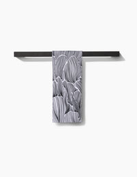 A black towel bar holds the Geometry Posh Petals Fresh Linen quick-drying towel, featuring an abstract black-and-white wavy line pattern, against a plain white background.