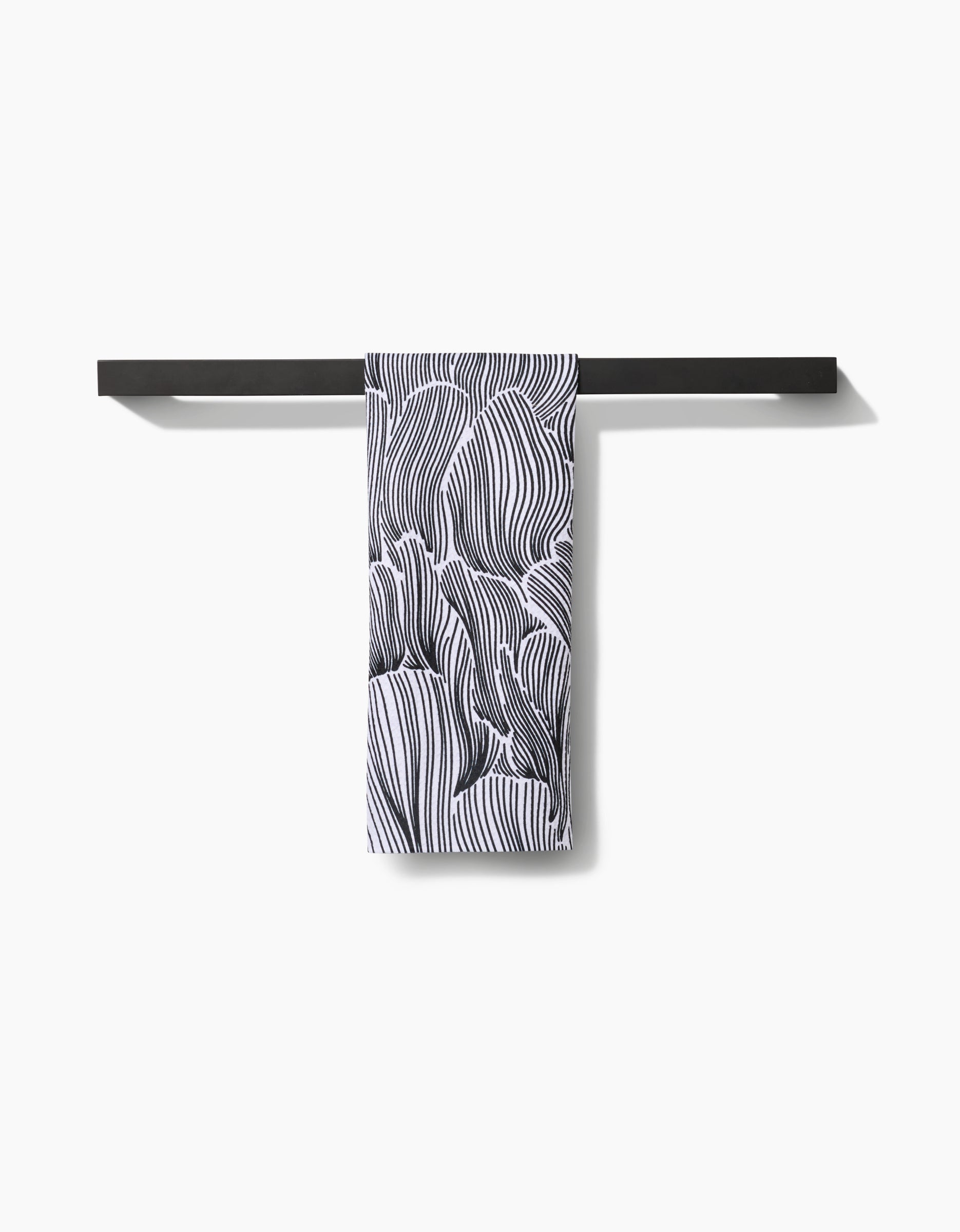 A black towel bar holds the Geometry Posh Petals Fresh Linen quick-drying towel, featuring an abstract black-and-white wavy line pattern, against a plain white background.