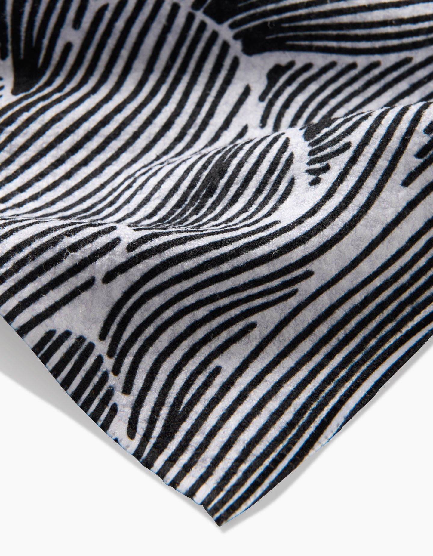 A close-up of the Geometry Posh Petals Fresh Linen tea towel displays its black and white wavy striped pattern, highlighting intricate details and a gently curled edge.
