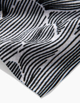 A close-up of the Geometry Posh Petals Fresh Linen tea towel displays its black and white wavy striped pattern, highlighting intricate details and a gently curled edge.