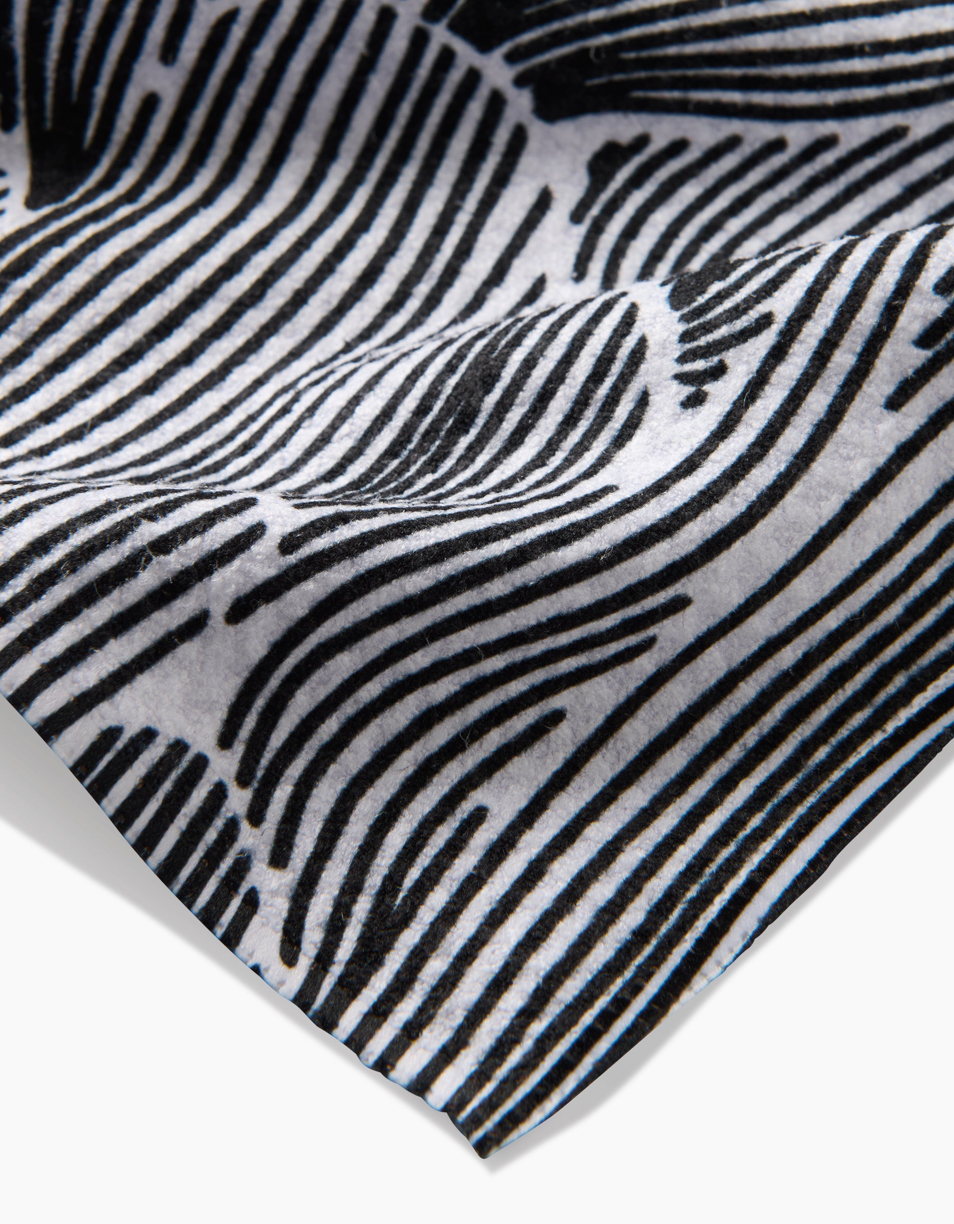 A close-up of the Geometry Posh Petals Fresh Linen tea towel displays its black and white wavy striped pattern, highlighting intricate details and a gently curled edge.