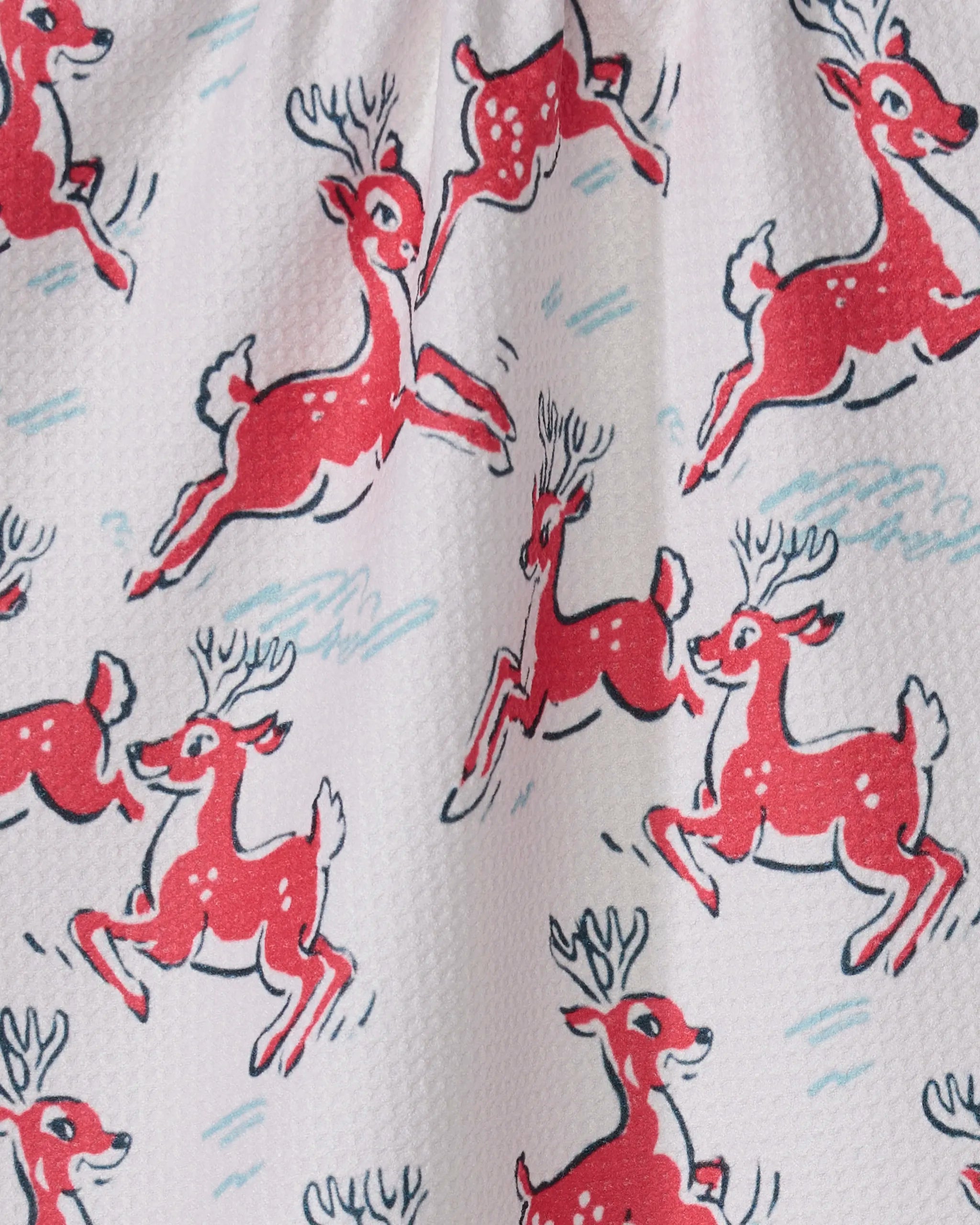 The “Prancing Reindeer” tea towel by Geometry features playful red reindeer with white spots and blue antlers on a light background, bringing charming, whimsical design to your kitchen.