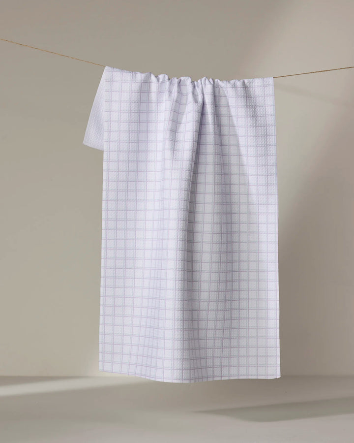 The Buy Guide’s Preppy - Mint Lilac tea towel, made from ultra-absorbent recycled materials with a mint and lilac grid design, hangs neatly on a thin clothesline against a neutral beige background.